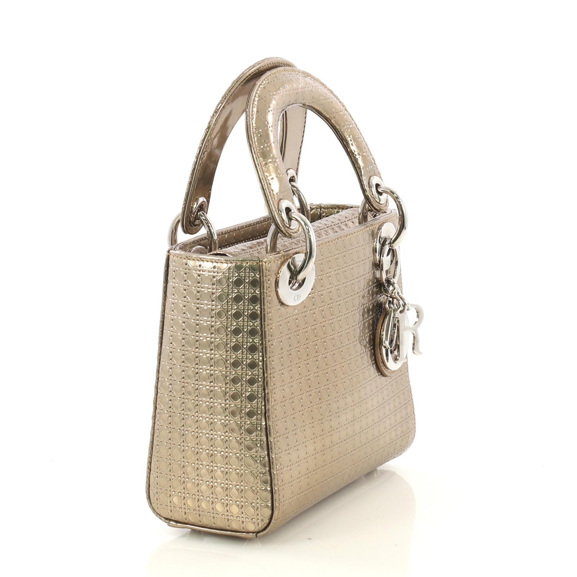 This Christian Dior Lady Dior Handbag Micro Cannage Perforated Calfskin Micro, crafted from gold cannage perforated calfskin leather, features short dual handles with Dior charms and silver-tone hardware. Its flap top closure opens to a gray leather