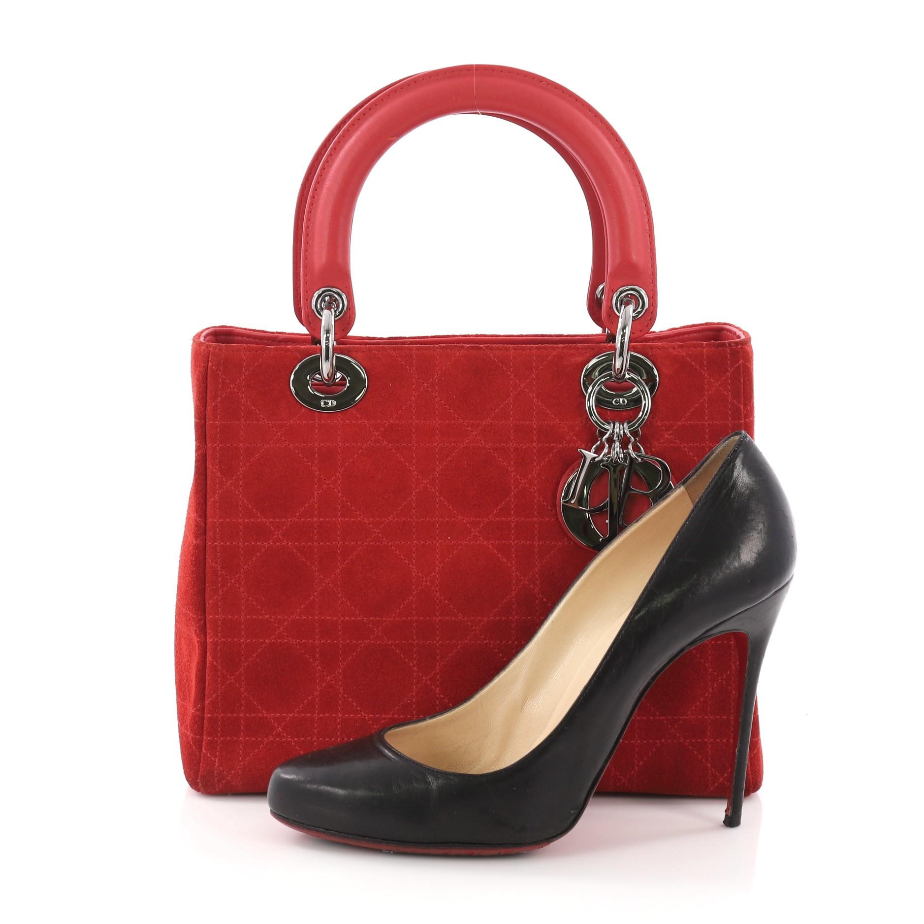 This Christian Dior Lady Dior Handbag Stitched Cannage Suede Medium, crafted in red stitched cannage suede, features short dual handles with Dior charms, protective base studs, and silver-tone hardware. Its top zip closure opens to a black fabric