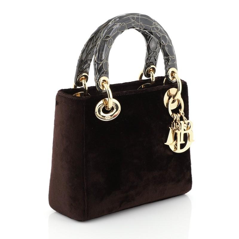 This Christian Dior Lady Dior Handbag Velvet Mini, crafted in brown velvet, features dual top handles, Dior charms, protective base studs, and gold-tone hardware. It opens to a metallic gold fabric interior with side zip pocket. 

Estimated Retail