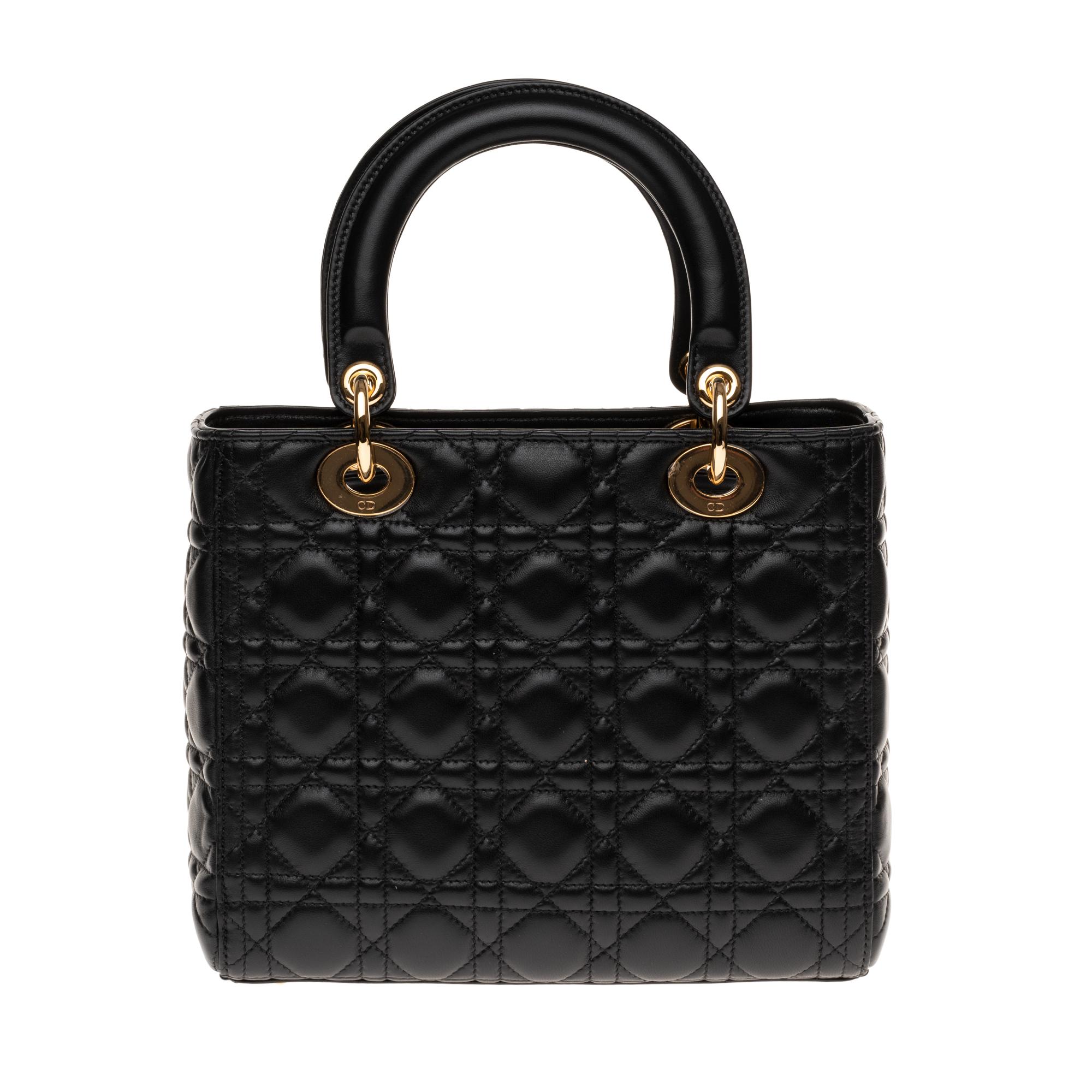 The classy and iconic shoulder bag Dior Lady Dior medium model in black cannage leather, gold metal hardware, double handle in black leather, removable shoulder strap handle in black leather allowing a handheld or shoulder or shoulder strap.

A