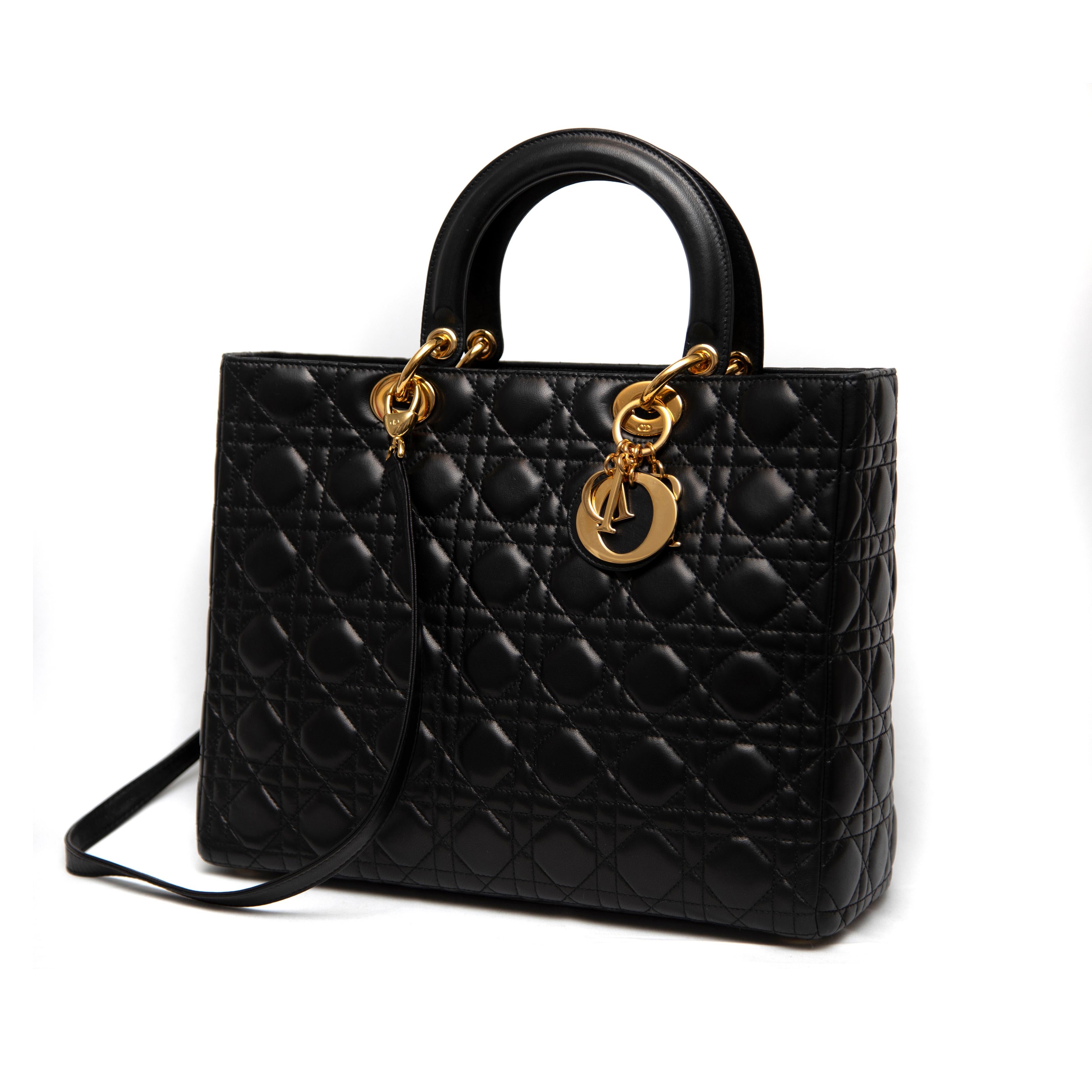 A luxurious classic from the late 1990s, this Christian Dior Large Lady Dior Handbag is crafted from sumptuous black quilted lambskin, showcasing the brand’s signature cannage stitching. The elegant design is elevated by gleaming gold-tone hardware,