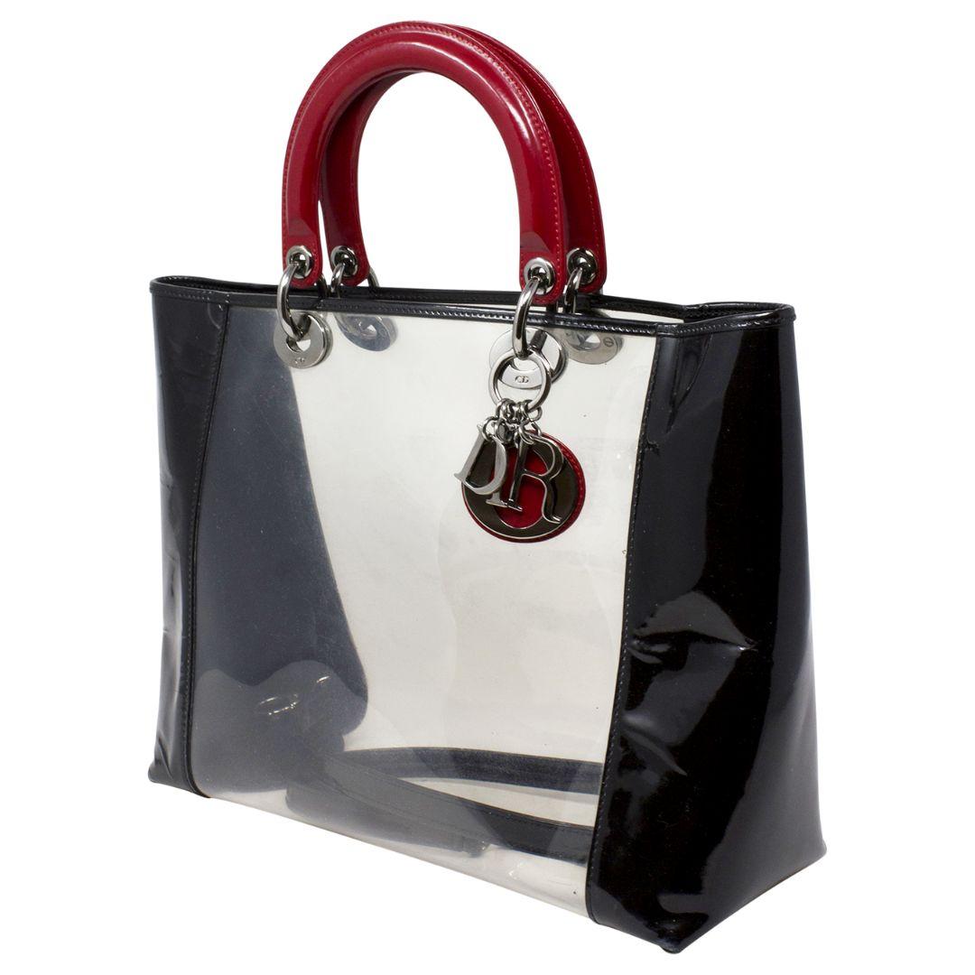 THIS CALLS FOR A POOL DAY! This fun and large Dior PVC Lady Dior has and iconic paneled black and clear PVC motif, with red double top handles and a fun red tonal DIOR charm. The open top opens up to a PVC interior. How fun to throw in your