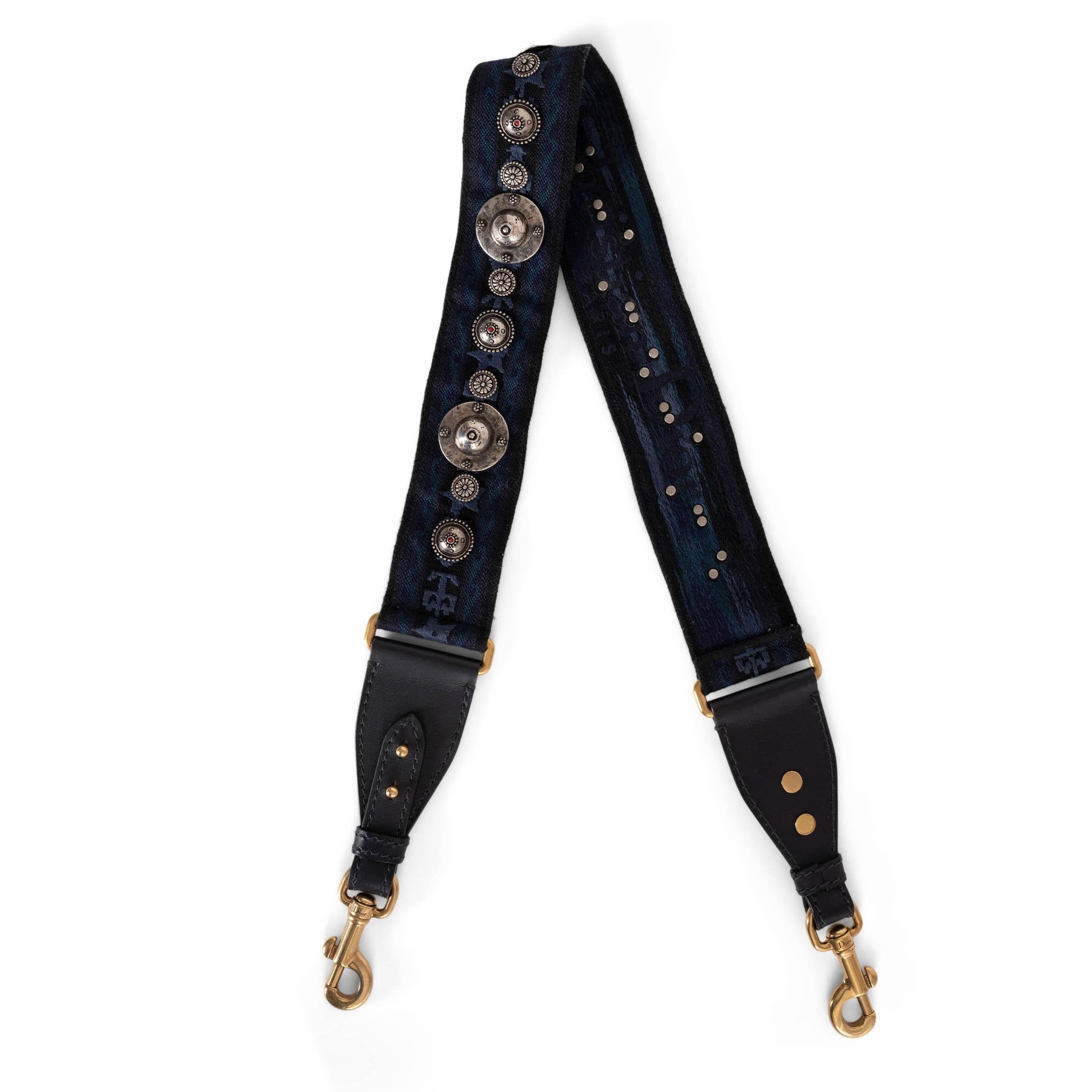 This 100% authentic Christian Dior bag strap in navy blue jacquard canvas adds a bold, Western-inspired touch to your favorite bag. Featuring antique silver-tone studs and gold-tone clasps, it blends contrasting metallic finishes for a striking