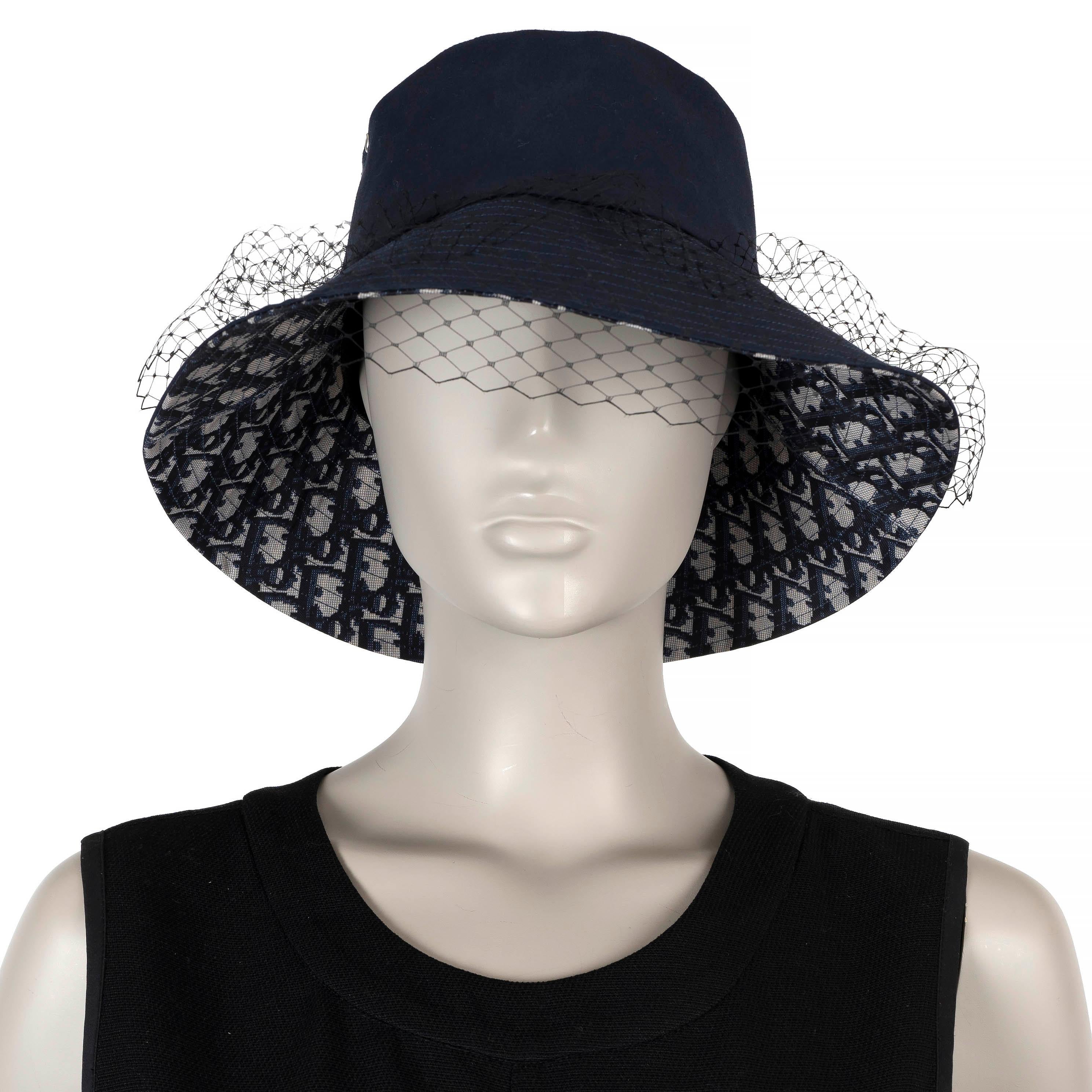 This 100% authentic Christian Dior Teddy-D Large Brim bucket hat is crafted from a blend of navy blue polyester (53%), cotton (42%), and polyurethane (5%), and features a delicate veil for a sophisticated touch. The brim is lined with the iconic