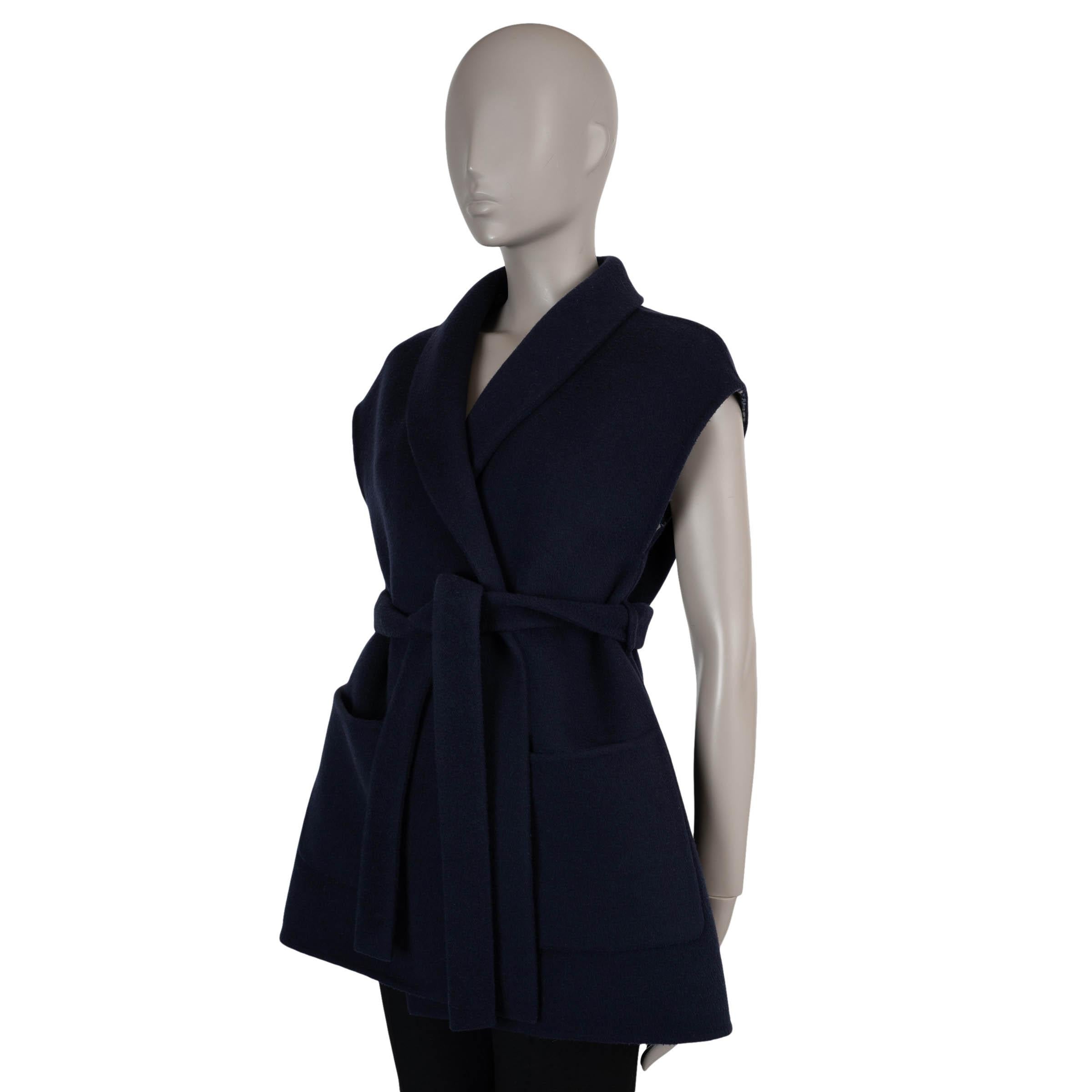 This 100% authentic Christian Dior sleeveless coat in navy blue double-face wool (99%) and silk (1%) blends timeless elegance with modern ease. Designed with a relaxed silhouette, it features a shawl collar, subtle cap sleeves, and two front patch