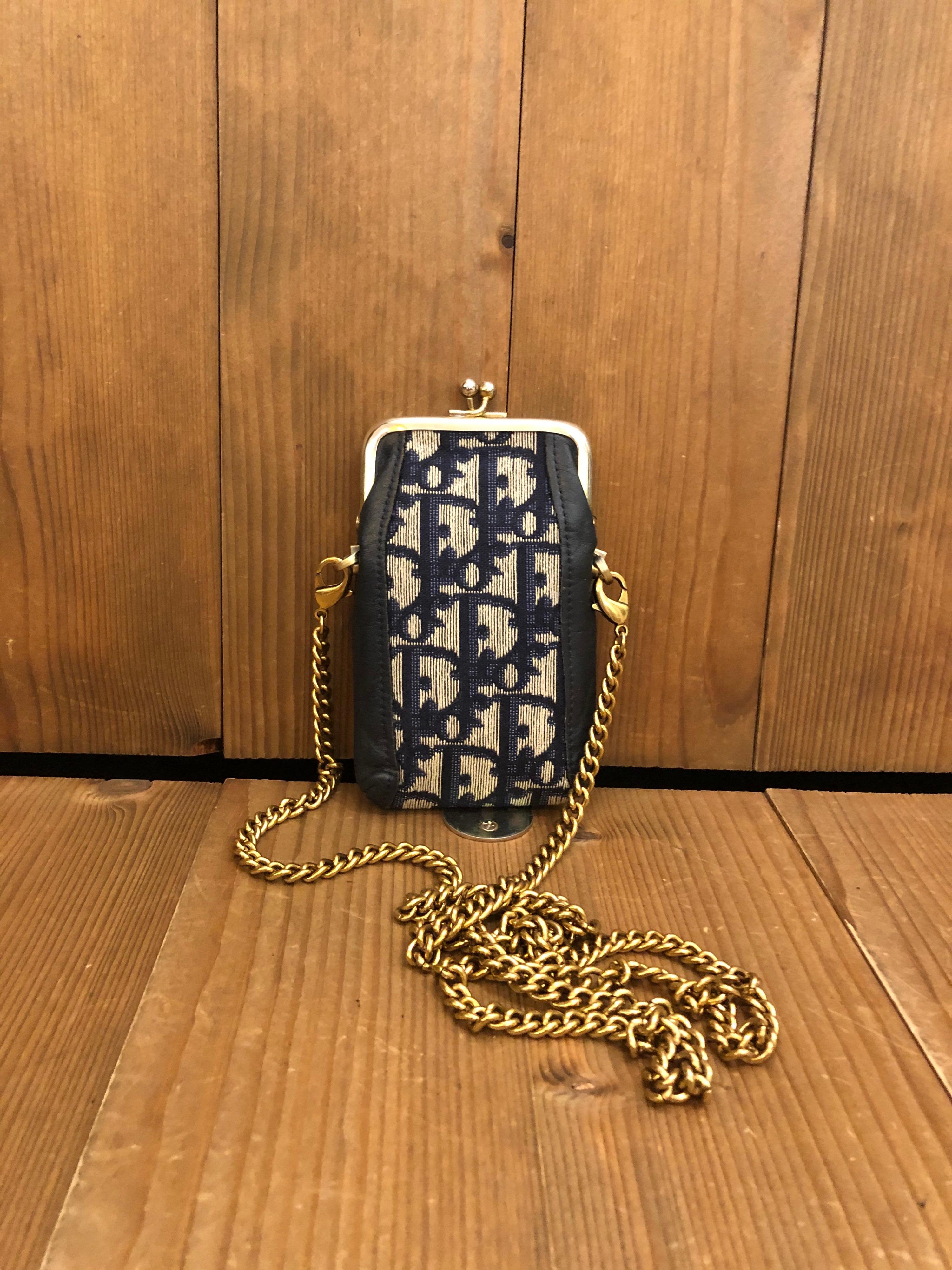 This vintage CHRISTIAN DIOR coin pouch is crafted of Dior signature Trotter Jacquard in navy and leather featuring a kiss clasp closure. It opens to a navy nylon interior. Third party hardware added on the sides to secure a gold toned chain.