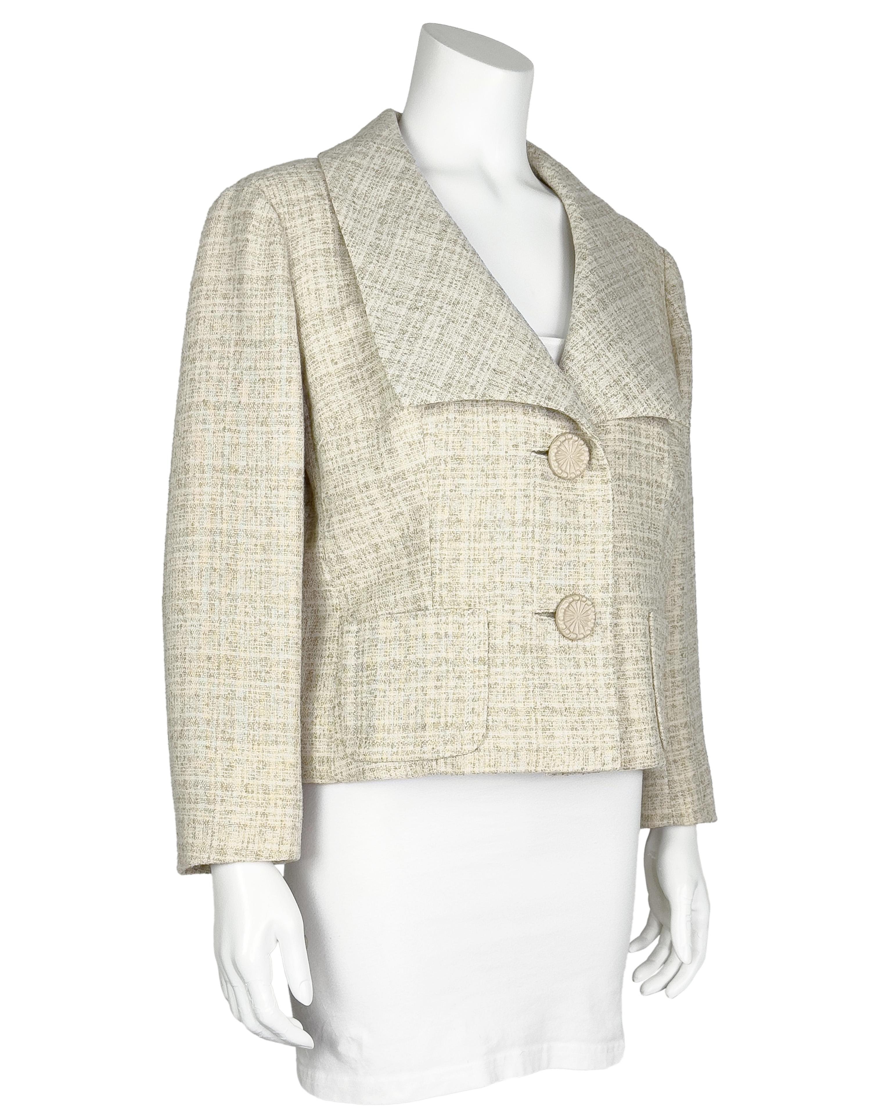 Chaqueta recortada en color crema de la marca Dior New York de los años 50, con amplio cuello cuadrado y bolsillos de parche delanteros. La chaqueta se abrocha con dos grandes botones de plástico texturizado y un broche oculto. Forrado en tejido