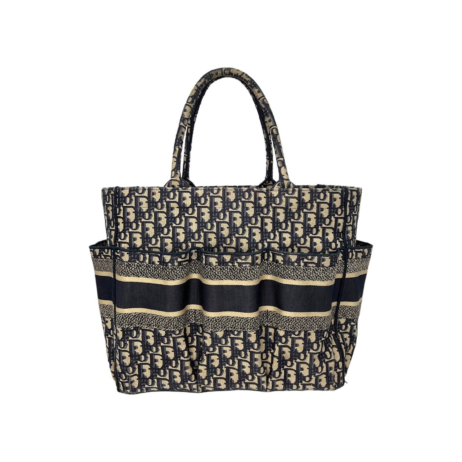 This Christian Dior Oblique Catherine Tote was made in Italy and it is finely crafted of a fully embroidered blue Dior Oblique motif canvas exterior. It has multiple slip pockets all around the exterior. It has dual rolled top handles. It features