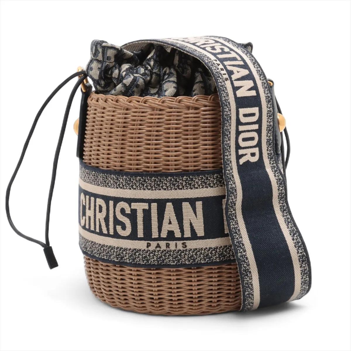 Le sac à bandoulière Christian Dior Oblique Rattan Canvas Bucket Shoulder Bag in Beige x Navy Blue est un mélange chic de design classique et de savoir-faire artisanal. Le motif Dior Oblique, emblématique de la marque, est reproduit sur la toile