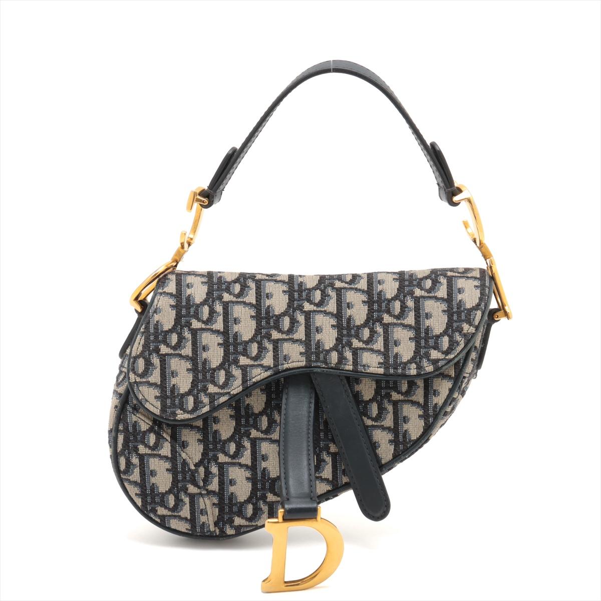 El bolso Christian Dior Oblique Saddle en azul marino es una pieza icónica que combina el diseño clásico con la elegancia moderna. Confeccionado en la emblemática lona jacquard Dior Oblique con ribetes de piel lisa, el bolso presenta la