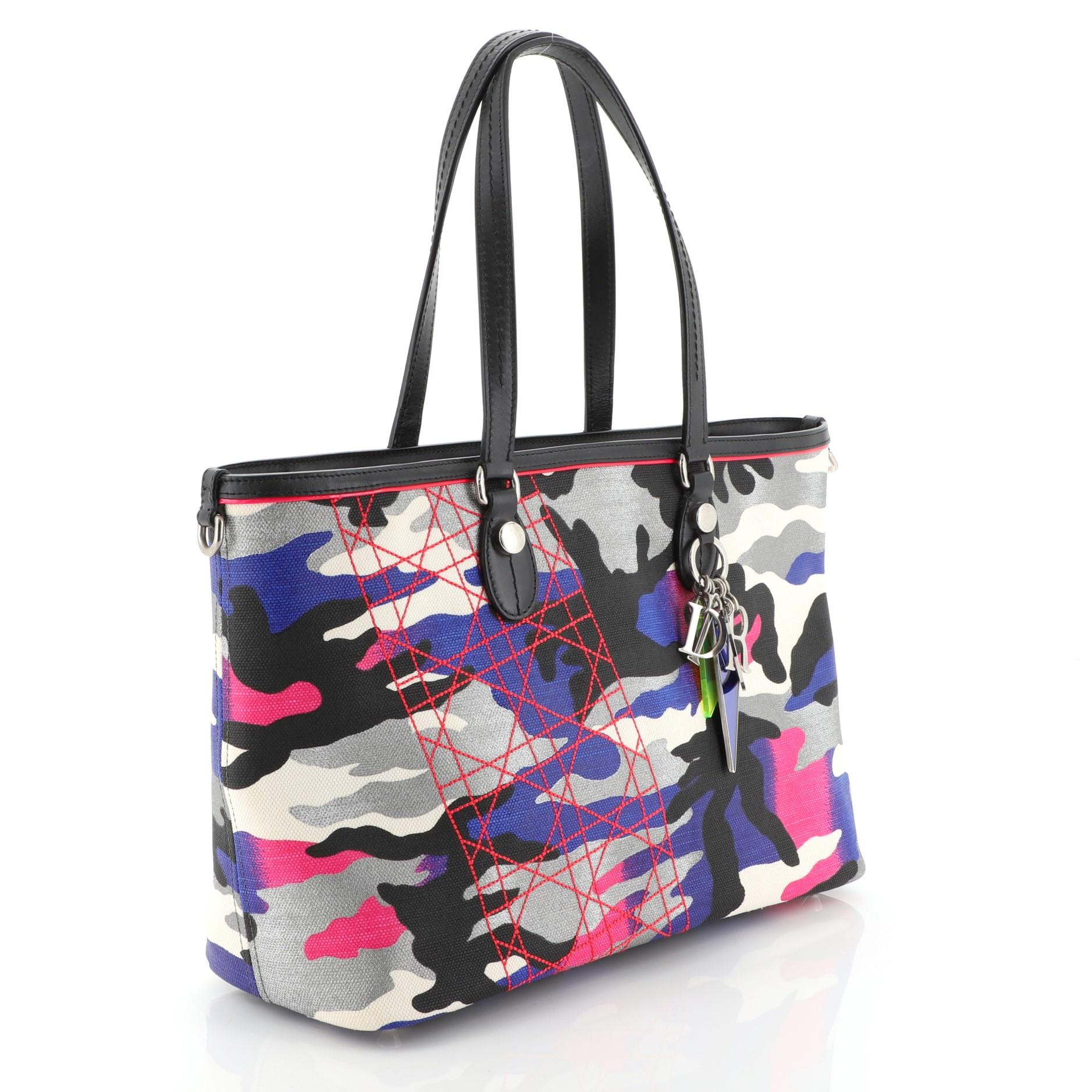 This Christian Dior Open Tote Limited Edition Anselm Reyle Camouflage Canvas Medium, crafted in blue and pink multicolor camouflage canvas, features dual flat leather handles, leather trim, and silver-tone hardware. Its zip closure opens to a black