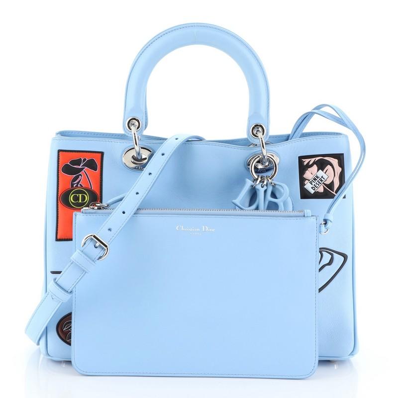 This Christian Dior Paradise Diorissimo Tote Calfskin Medium, crafted from blue calfskin leather, features short dual handles with Dior charms, side snap buttons, protective base studs, and silver-tone hardware. Its magnetic snap closure opens to a
