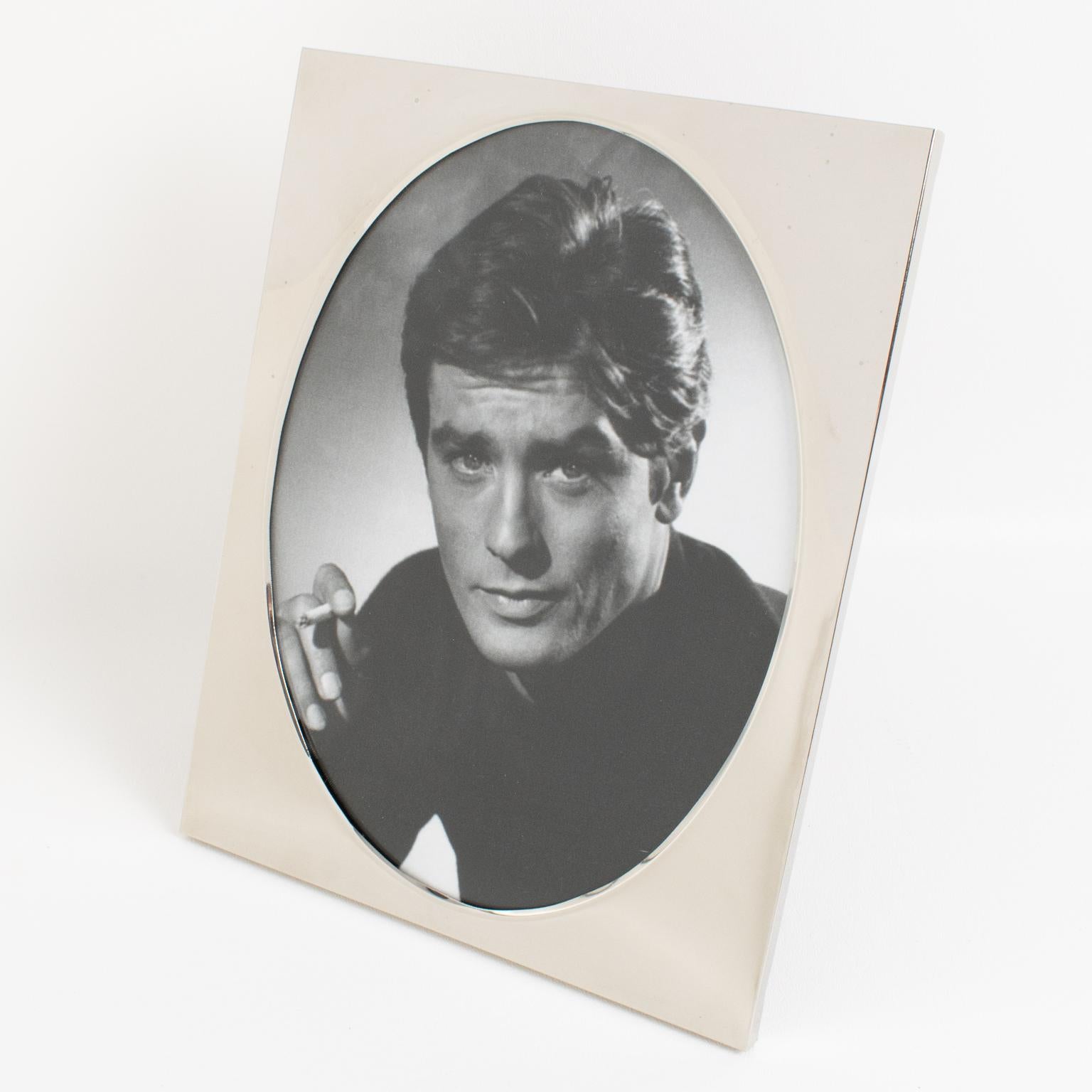 This exquisite Christian Dior Paris chromed metal picture frame features a plain and minimalist geometric shape with an oval picture view. The rare piece was crafted in France circa 1970. The back and easel are made of glossy, varnished wood. The