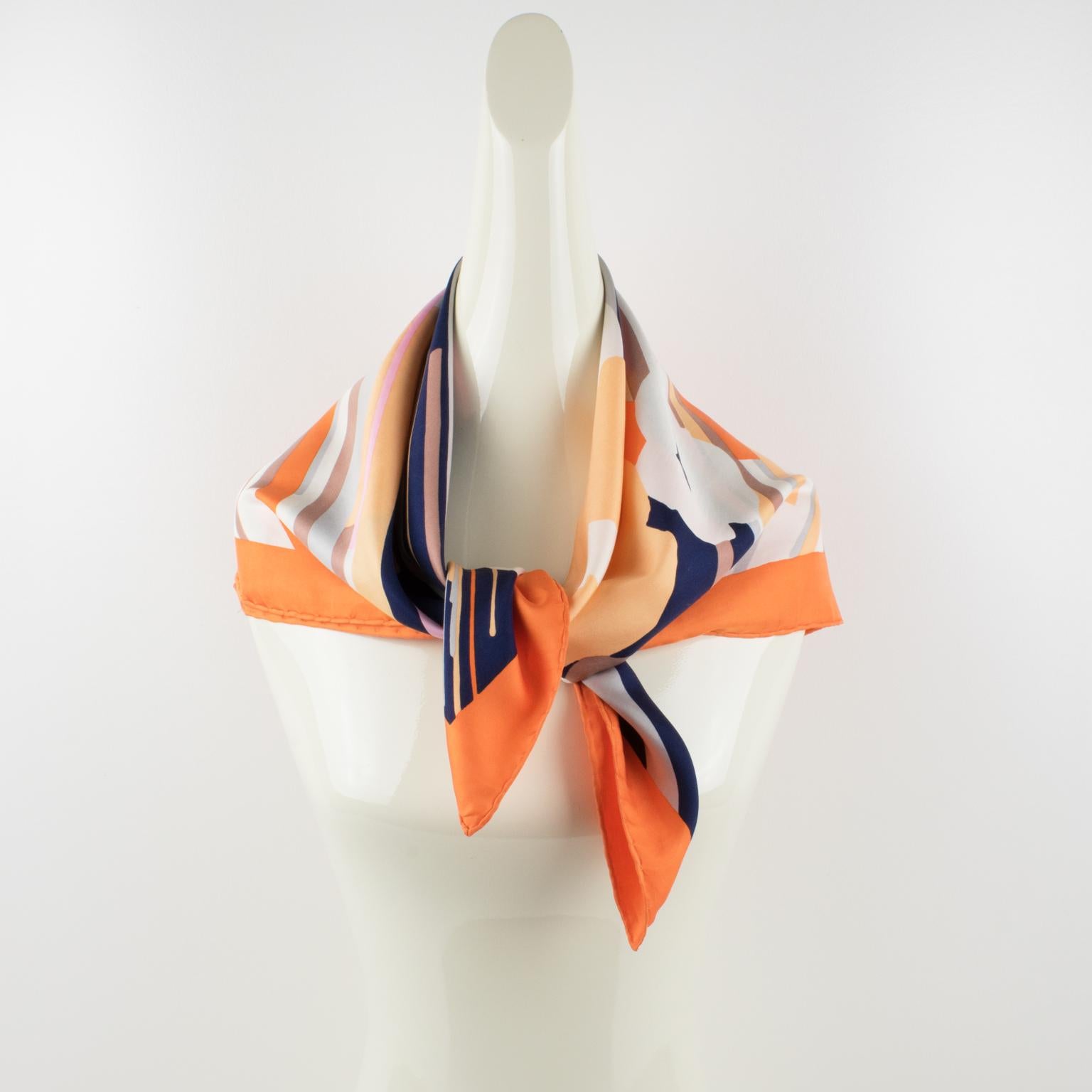 This elegant silk scarf by Christian Dior Paris boasts a geometric and floral print pattern. The combination of colors is bright and vibrant with navy blue, purple, pink, gray, white, salmon-orange, and a bright orange border. The piece is signed