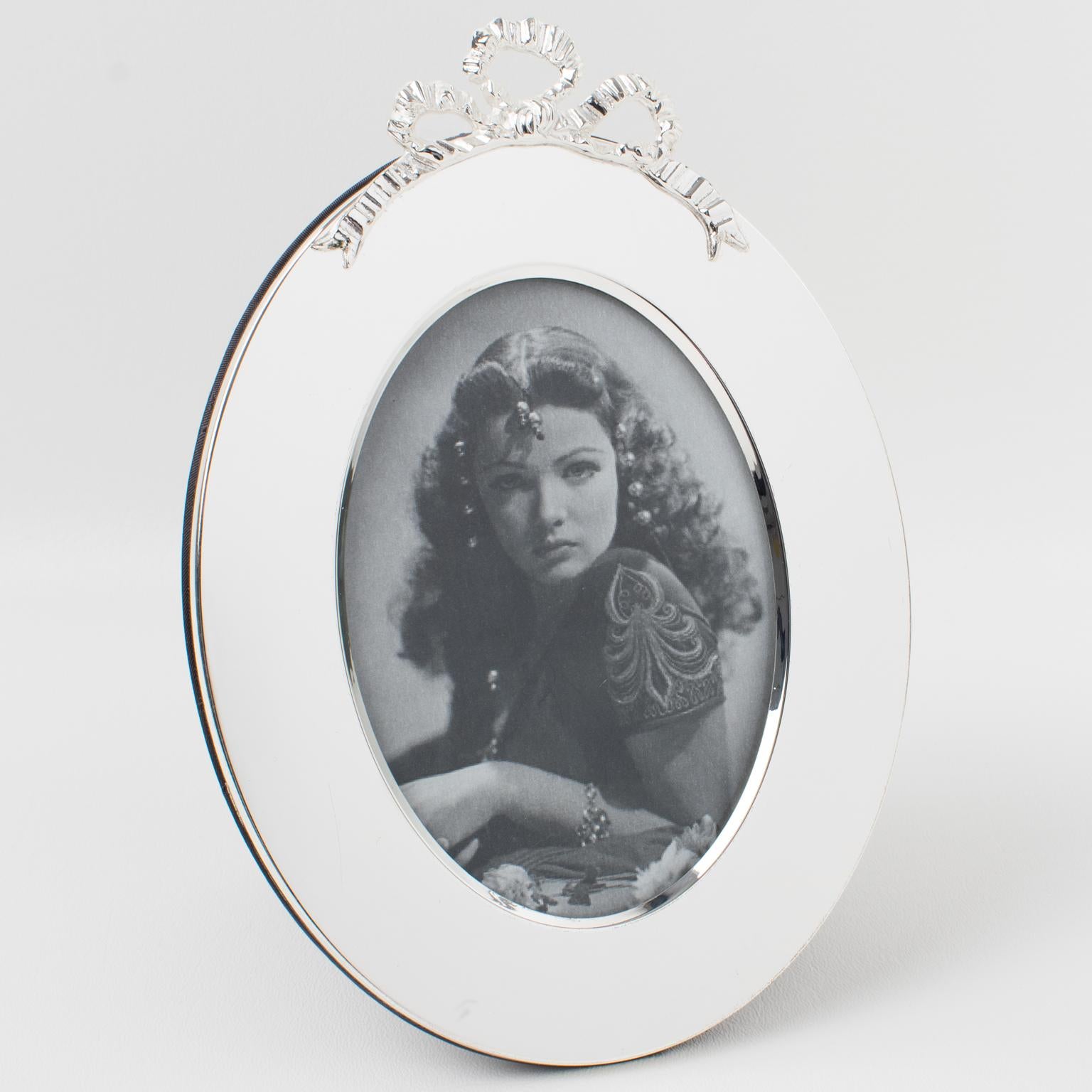 Quite a romantic Christian Dior Paris silverplate picture photo frame. Ovoid shape with a lovely bow decor on the top. The back and easel are in black silk fabric with the 