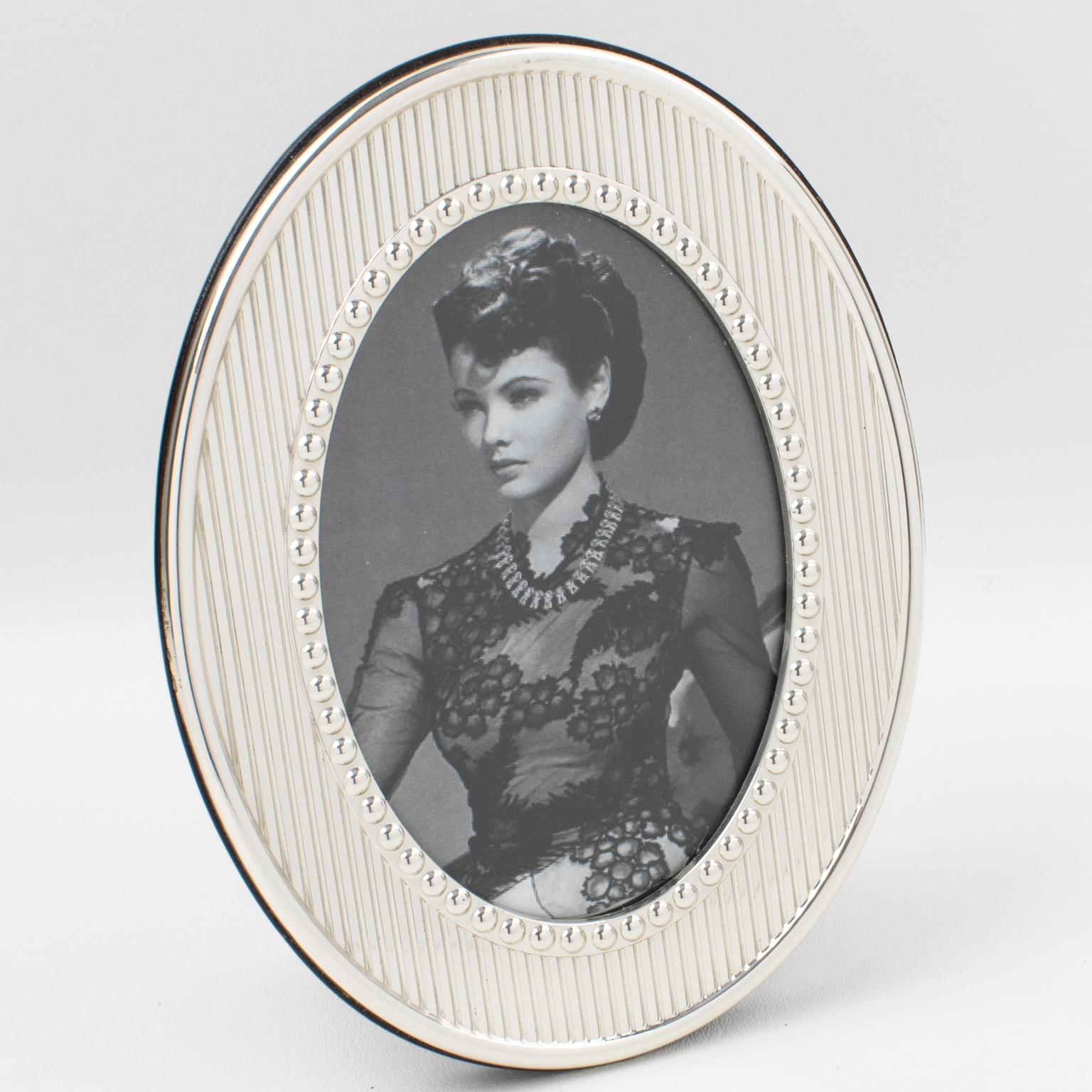 Christian Dior Paris designed this elegant sterling silver picture photo frame for its Home Collection. The oval shape has stripes and beveling patterns all around. The back and easel are in high gloss varnish dark wood. The frame is hot stamped on