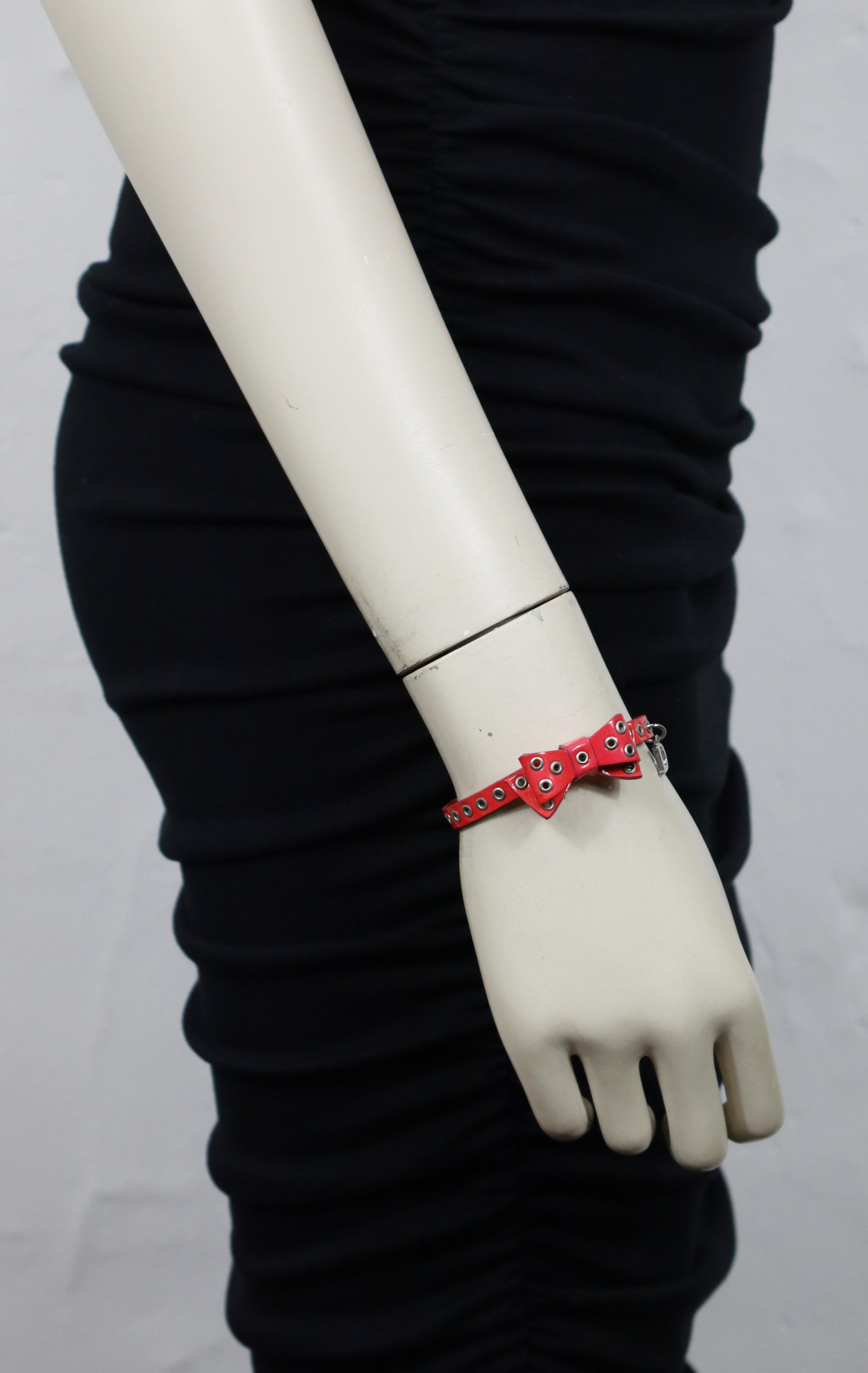 **** INFORMATION IMPORTANTE : La vraie couleur est le ROSE, PAS le rouge ****

Bracelet en cuir verni rose CHRISTIAN DIOR avec œillets argentés et breloque D dangle piercing like.

Fermeture réglable avec fermoir en forme de homard.

Embossé