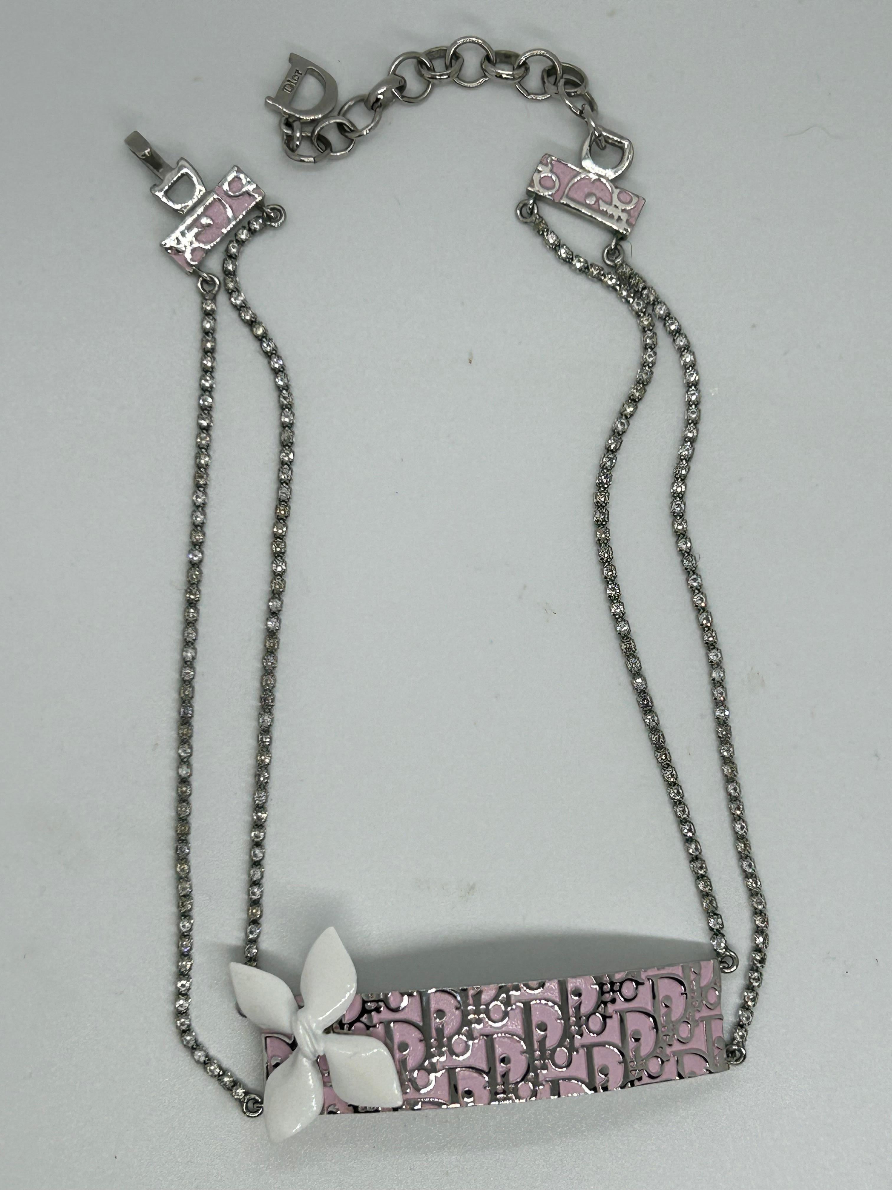 A Gorgeous pink logo trotter choker from Christian Dior.
This beautiful necklace is a real pretty piece.
Pink pastel background with silver Dior logo and a pretty white enamel petal on one corner .
Two chains with diamantés crystals and a hook