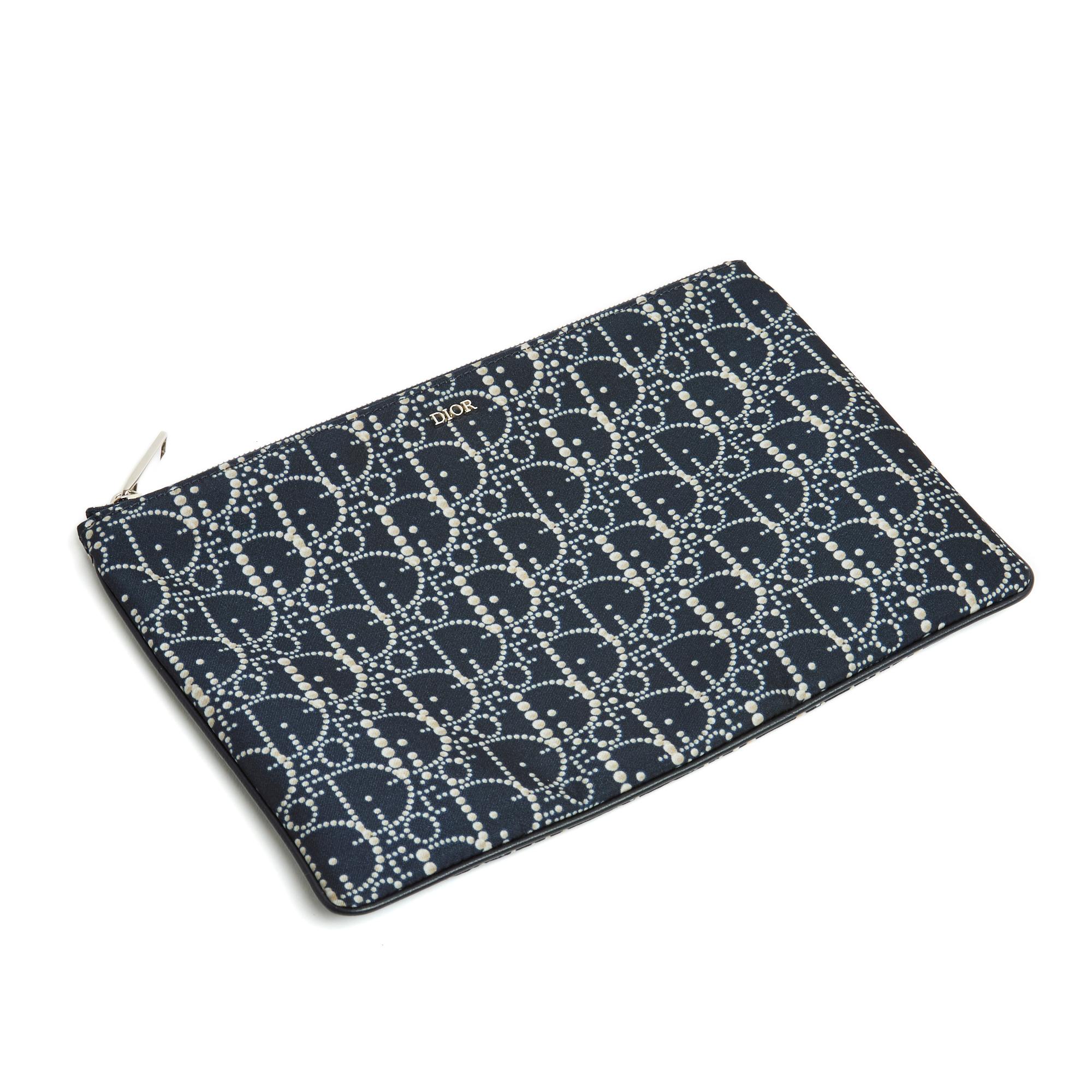 Pochette Dior Daily model en toile satinée avec motif Oblique en perles et passepoil en cuir noir, petit logo Dior en métal argenté sur le devant, intérieur en toile noire avec griffe et numéro unique sur le cuir, fermeture par un long zip en métal