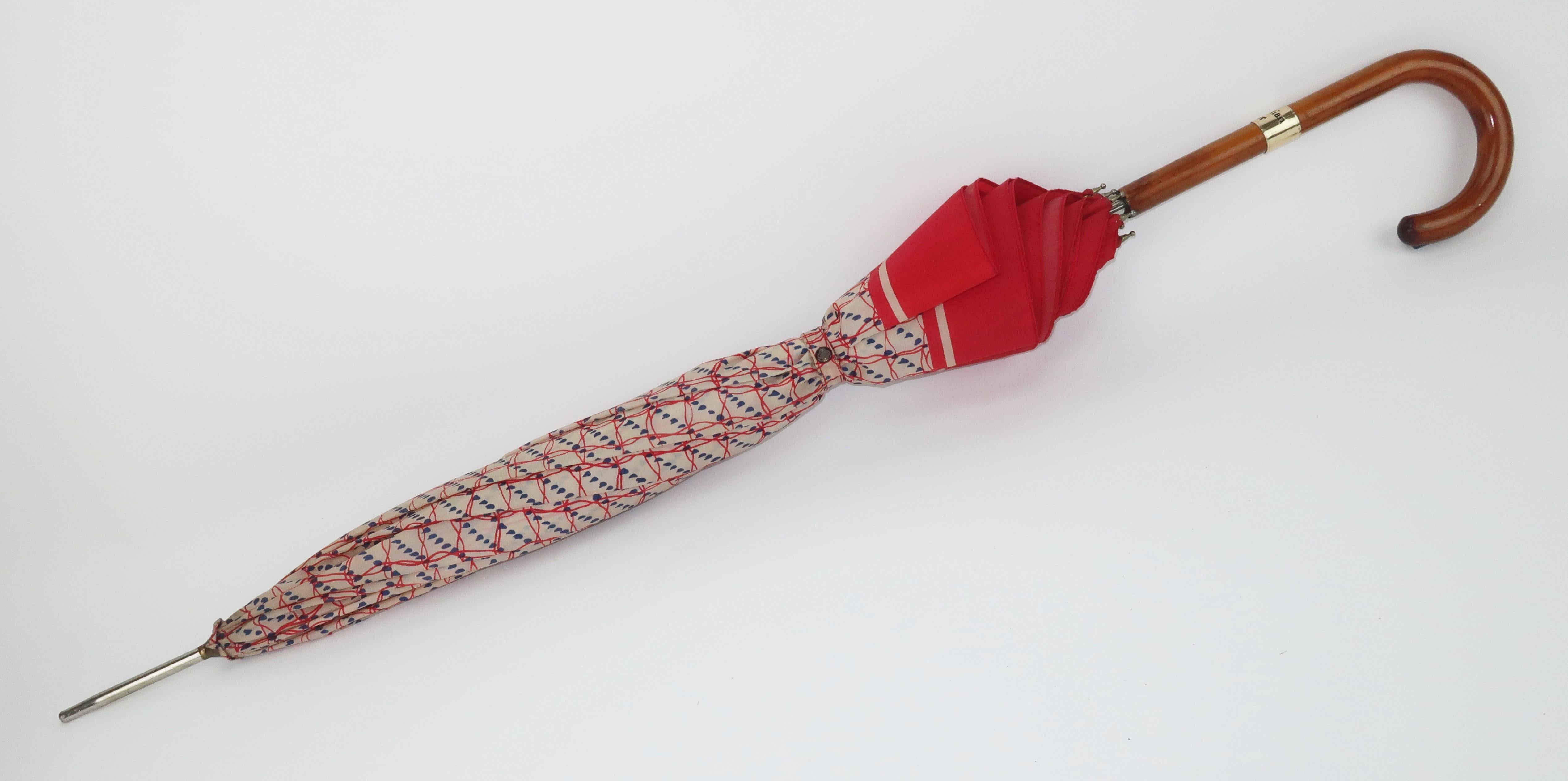 This 1970's Christian Dior red, ecru white and blue nylon umbrella is a fun blast from the past.  Outfitted with a sturdy old school wooden handle with an abstract print that is reminiscent of rain drops and incorporates the Christian Dior name. 