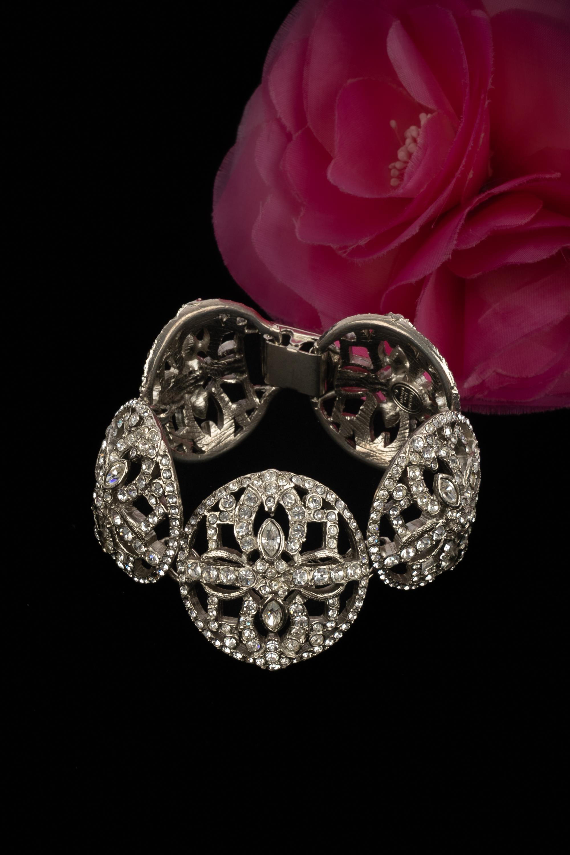 DIOR - Pulsera articulada de metal plateado calado, adornada con brillantes de diferentes tamaños. Una Colección circa 2000 bajo la dirección artística de John Galliano.

Estado:
Muy buen estado

Dimensiones:
Longitud: 18 cm - Anchura: 3,5