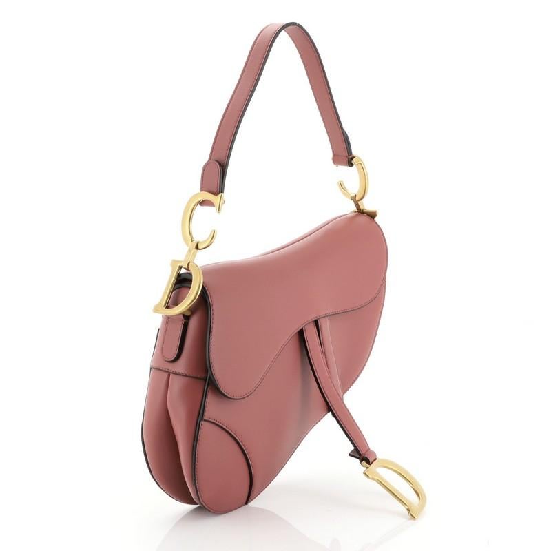 This Christian Dior Saddle Handbag Leather Medium, crafted from pink leather, features a top handle adorned with metal 'CD' hardware and aged gold-tone hardware. Its fold over top opens to a pink suede interior with zip pocket.

Condition: