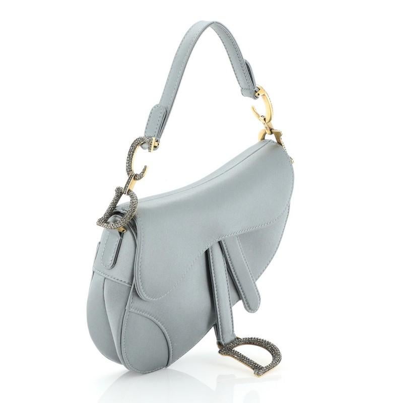 This Christian Dior Saddle Handbag Satin with Crystals Mini, crafted from gray satin, features a top handle adorned with studded metal 'CD' finishing, saddle-shaped silhouette and aged gold-tone hardware. Its fold-over top opens to a gray satin