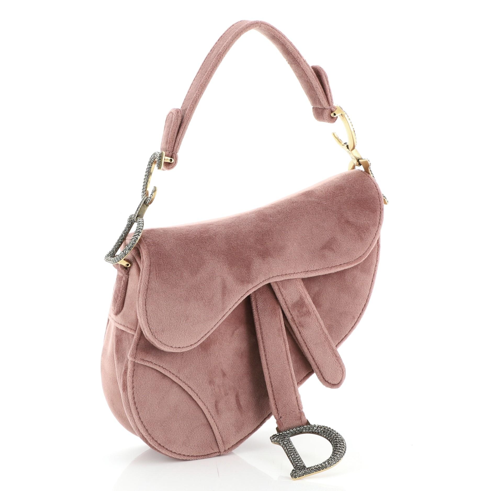 This Christian Dior Saddle Handbag Velvet with Crystals Mini, crafted from pink velvet, features a top handle adorned with metal 'CD' hardware and aged gold-tone hardware. Its fold over top opens to a pink suede interior with zip pocket. 

Estimated