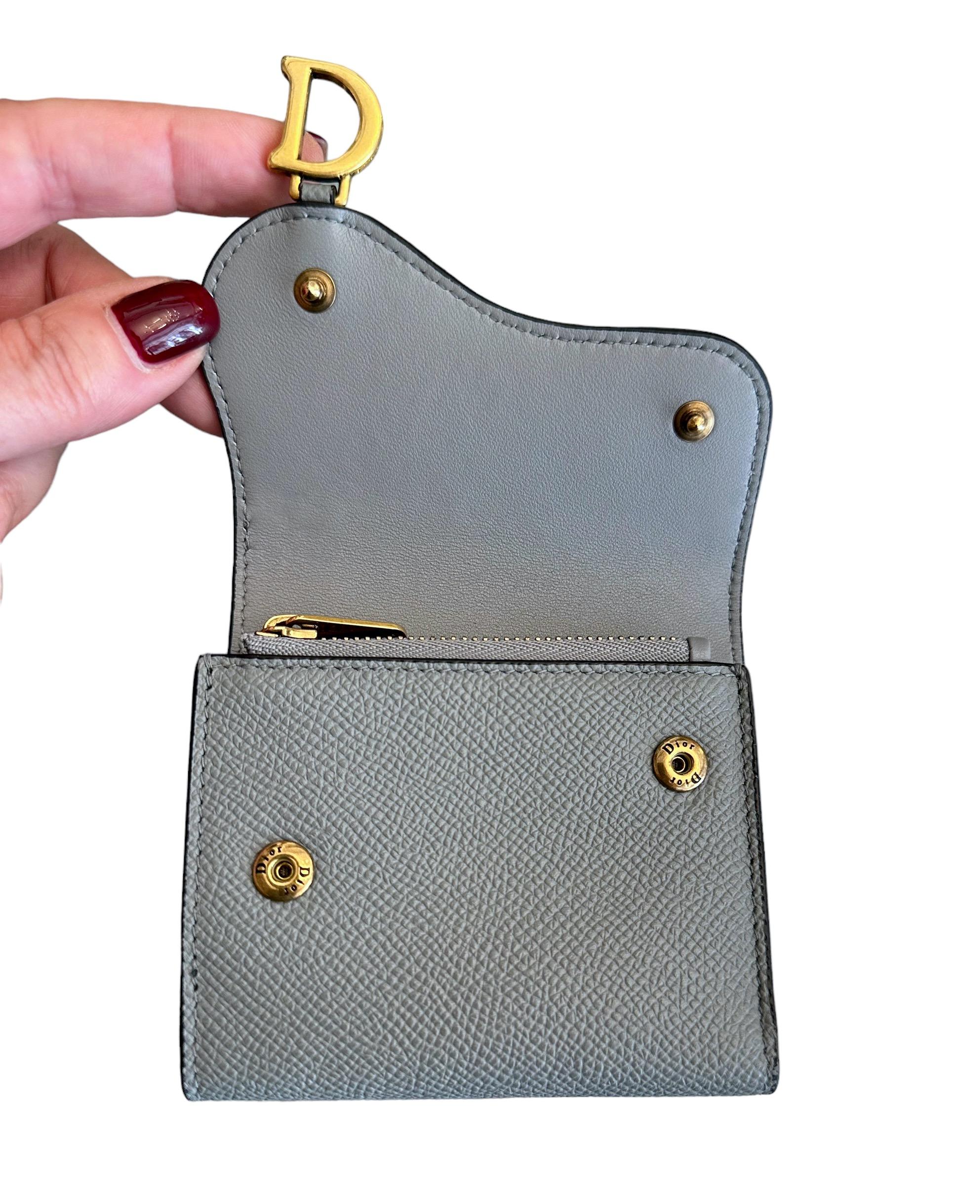 This pre-owned  Saddle Lotus wallet is part of the Saddle Collection from the house of Dior.
It is crafted in a gray stone color grained calfskin leather and is in perfect condition.
It features the iconic asymmetrical flap and antique gold-finish