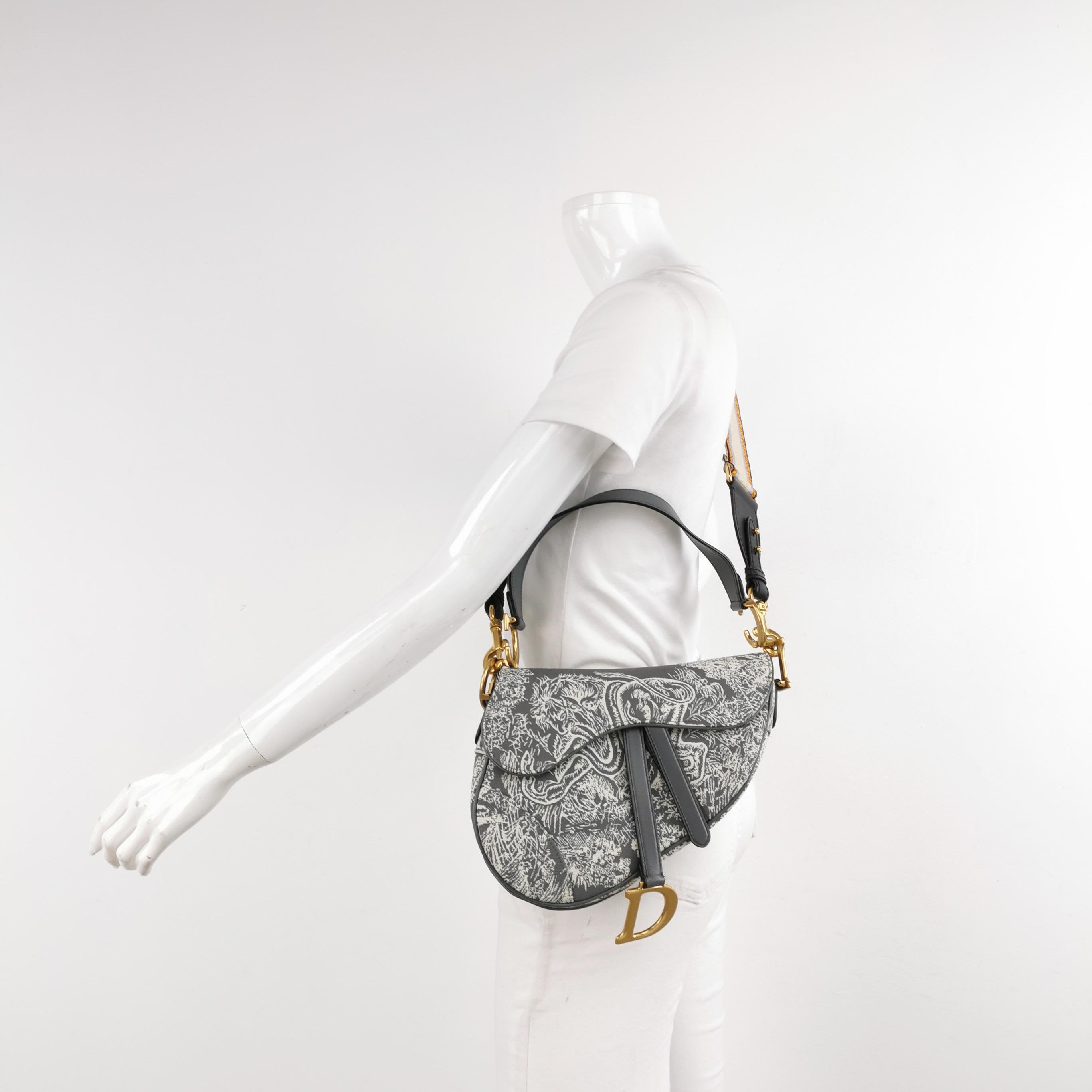 Este bolso Dior Saddle de tamaño mediano está fabricado en lona con estampados de selva tropical y estampados de animales como el tigre, la serpiente y el mono. Incluye una solapa magnética y luce una firma de CD con acabado en oro envejecido a cada