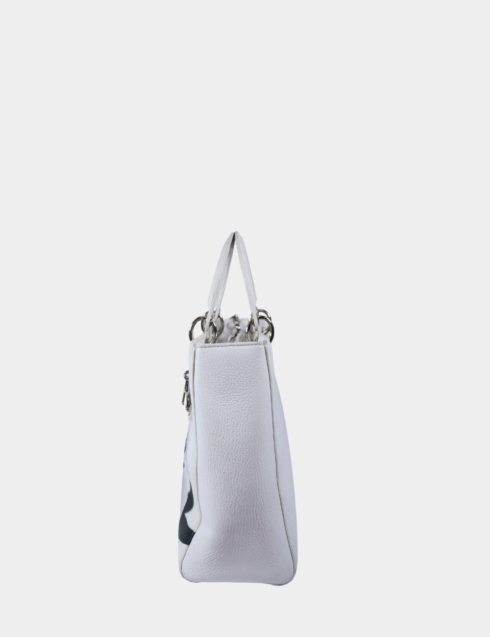 Make a bold, elegant statement with this Christian Dior White Leather Tote, featuring a stunning oversized floral print and signature silver-tone Dior letter charms. Crafted from luxurious pebbled leather, this structured tote exudes modern romance