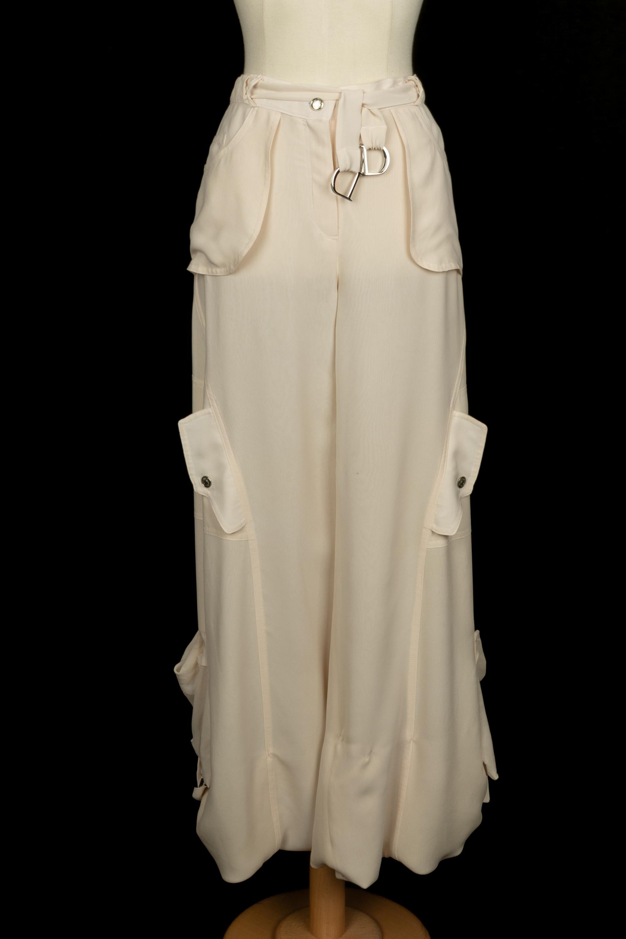 GALLIANO - (Fabriqué en France) Ensemble en crêpe de soie ivoire. Top à manches volantées, décolleté et laçage dans le dos. Pantalon avec des éléments en métal argenté. Taille 36FR indiquée. A Collectional circa 2003 sous la direction artistique de