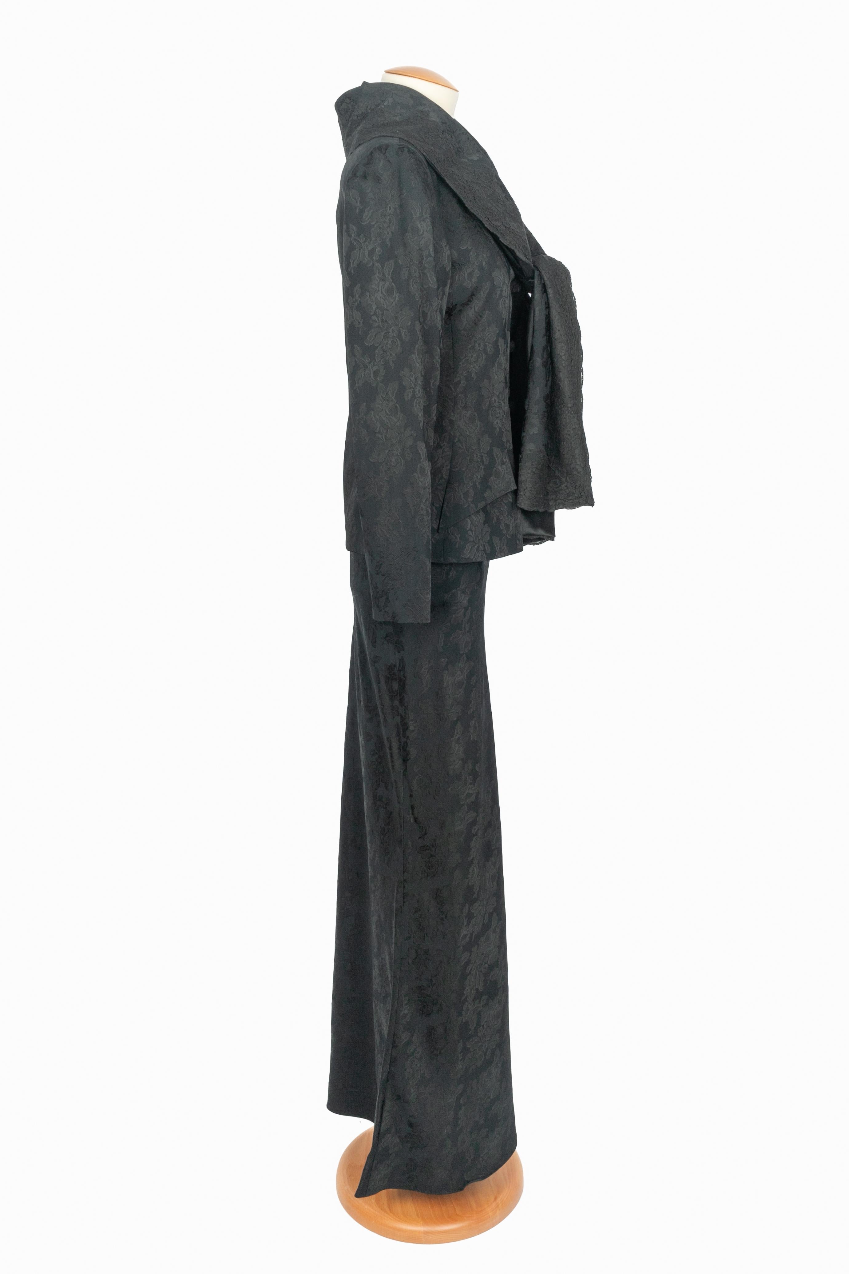 DIOR - (Made in France) Completo in jacquard nero con motivo floreale, composto da una giacca con collo a sciarpa ricamato in pizzo e cintura, e da una gonna lunga abbinata. Taglia 38FR indicata. Collezione Autunno-Inverno 1998 sotto la direzione