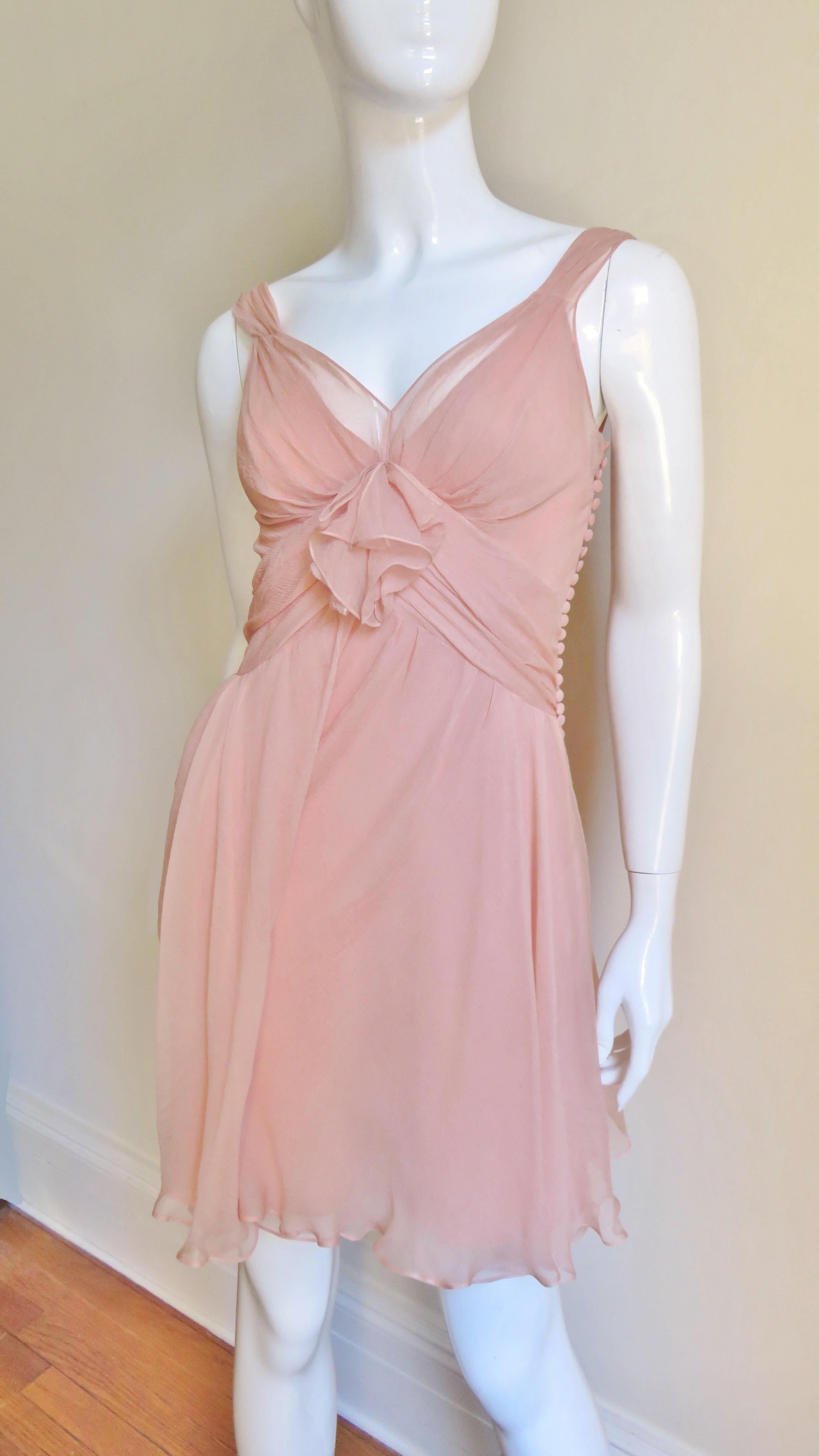 A gorgeous feminine peach silk dress from Christian Dior. It has ruched shoulder straps, bodice, and waist and a deep plunging back.  The full skirt has side draping and there are signature small silk covered buttons and loops along one side of the