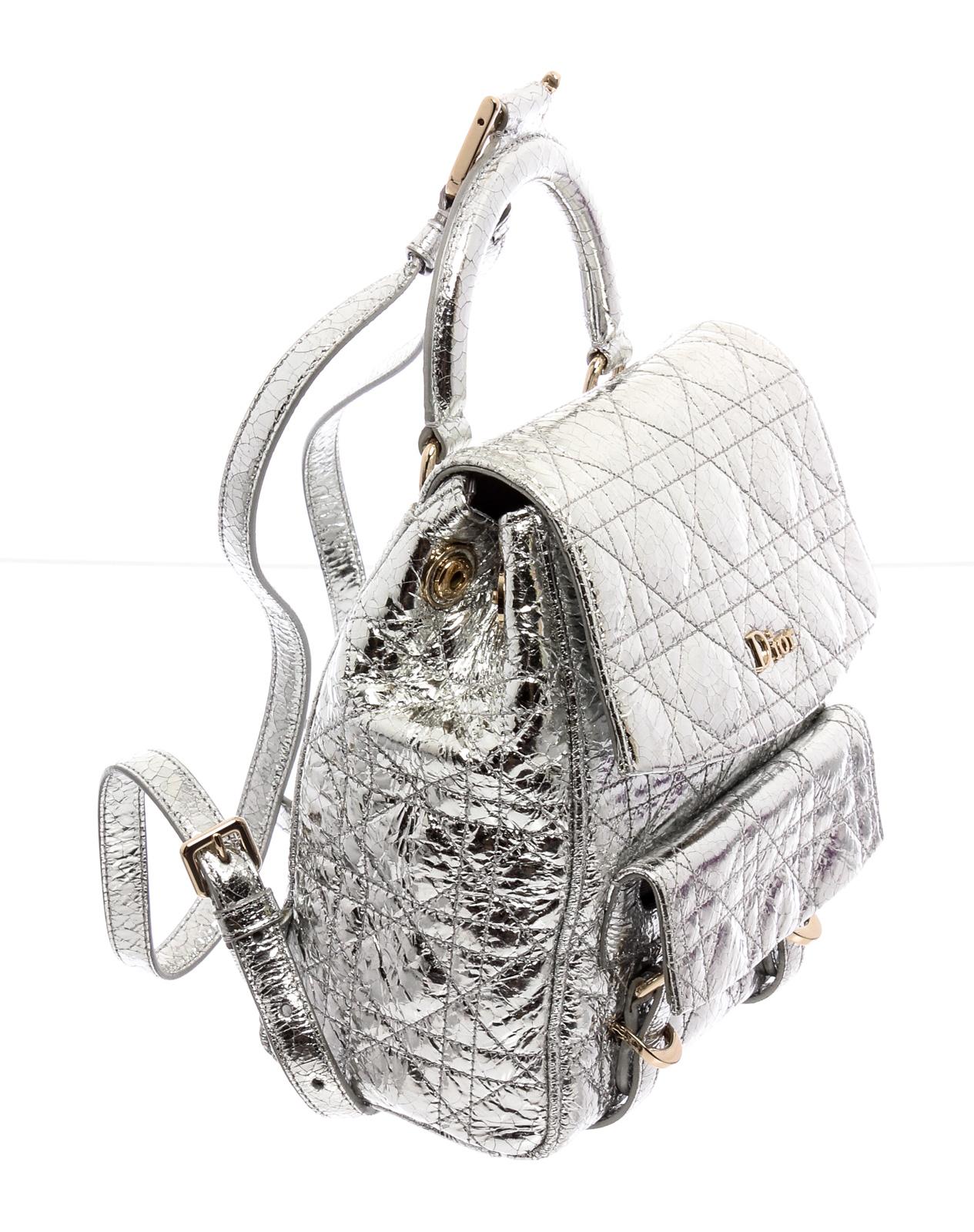 Dior Stardust backpack with gold-tone hardware, dual adjustable flat shoulder straps, single top handle with logo adornment, single pocket at back, single pocket at front with dual buckle closures, logo adornment at front flap, tonal grosgrain