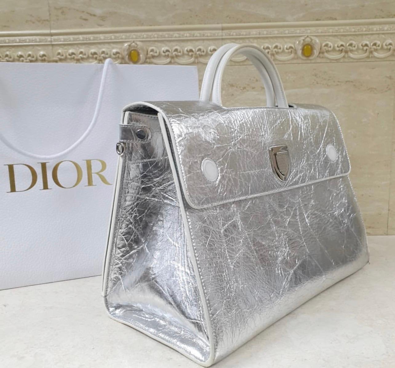 This fashionable bag from Christian Dior is a tote with a sleek and contemporary feel. The bag features a highly structured silhouette and statement hardware. 
The crescent shaped push closure draws the eye and even has the cannage pattern etched in
