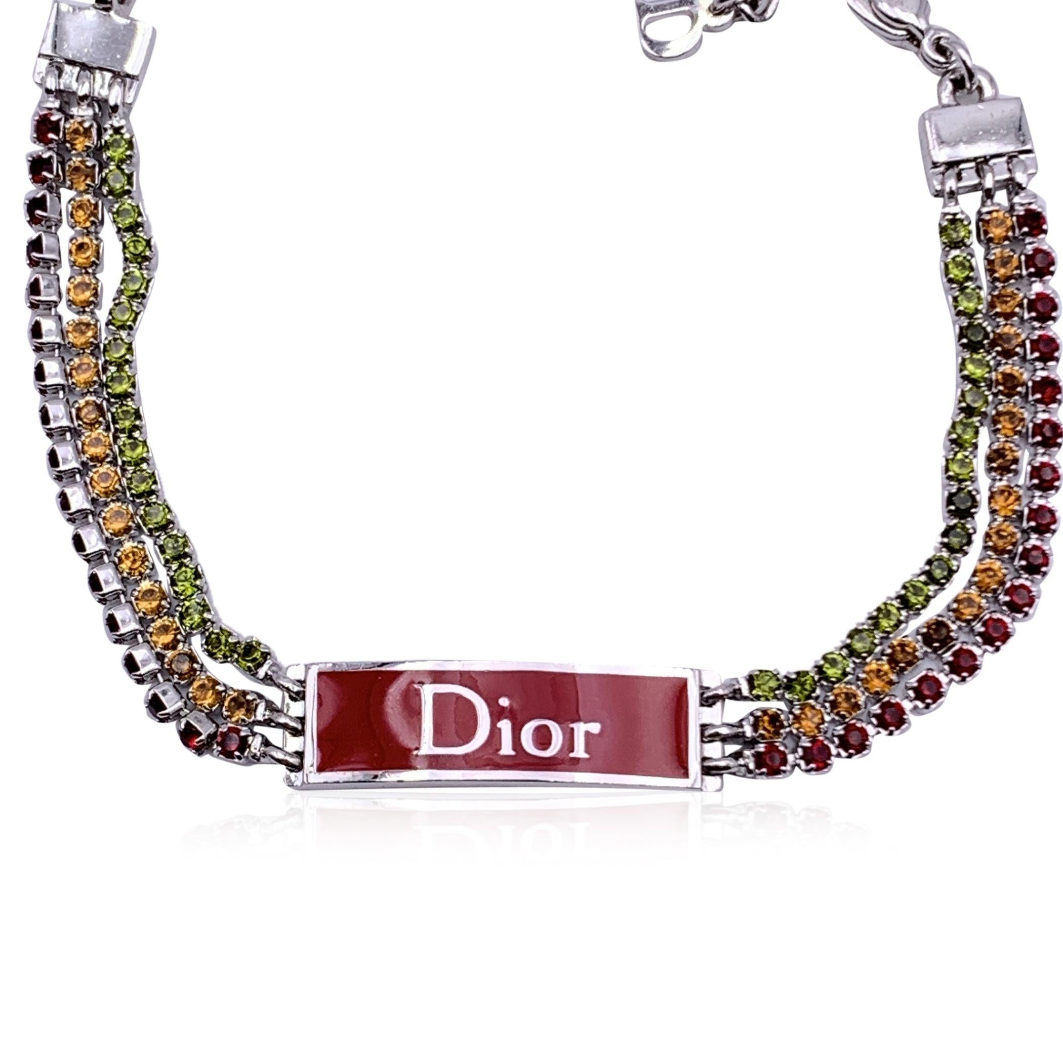 Bracelet Christian Dior Rasta avec 3 rangées de strass rouges, orange et verts avec plaque en émail rouge du logo Dior. Métal argenté. Fermeture en homard. Longueur totale : 8.5 inches - 21.6 cm. La mention 