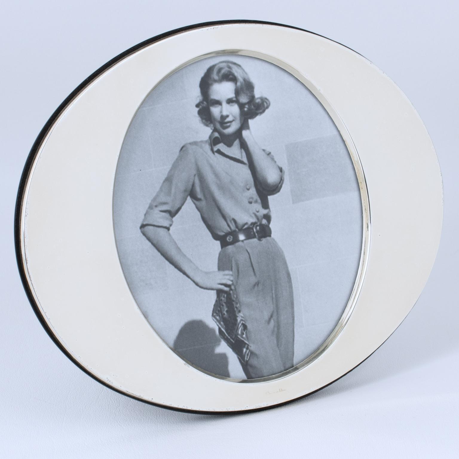 Este refinado marco de fotos Christian Dior París de plata de ley tiene una forma ovalada con el emblemático logotipo CD estilizado. La pieza se fabricó en Francia hacia 1980. La parte trasera y el caballete son de madera tropical de alto brillo. La