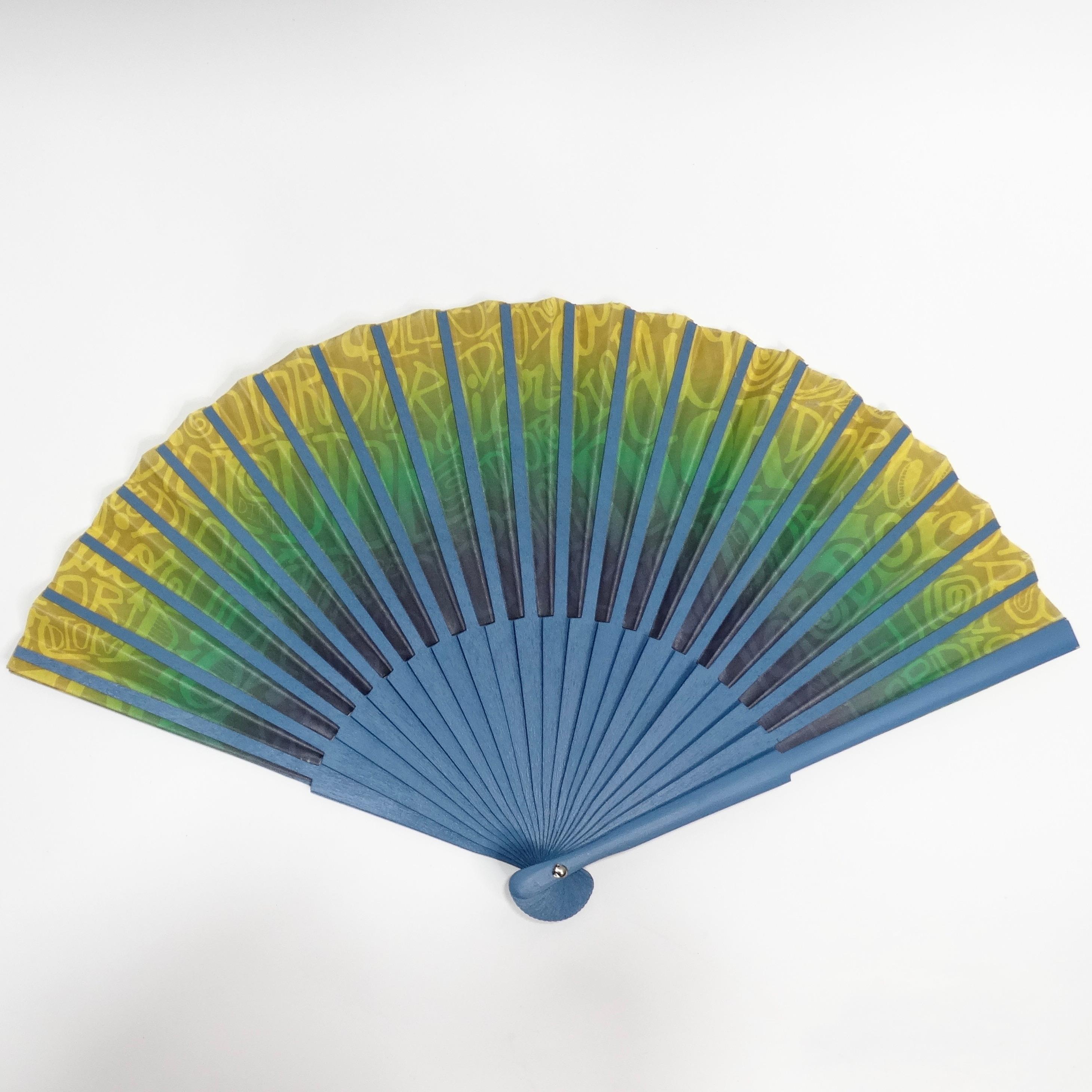 Introducing the Christian Dior Stussy Folding Fan, an extraordinary piece born from the collaboration between two iconic brands. This folding fan features a vibrant blue, green, and yellow gradient that transitions beautifully across the pleated