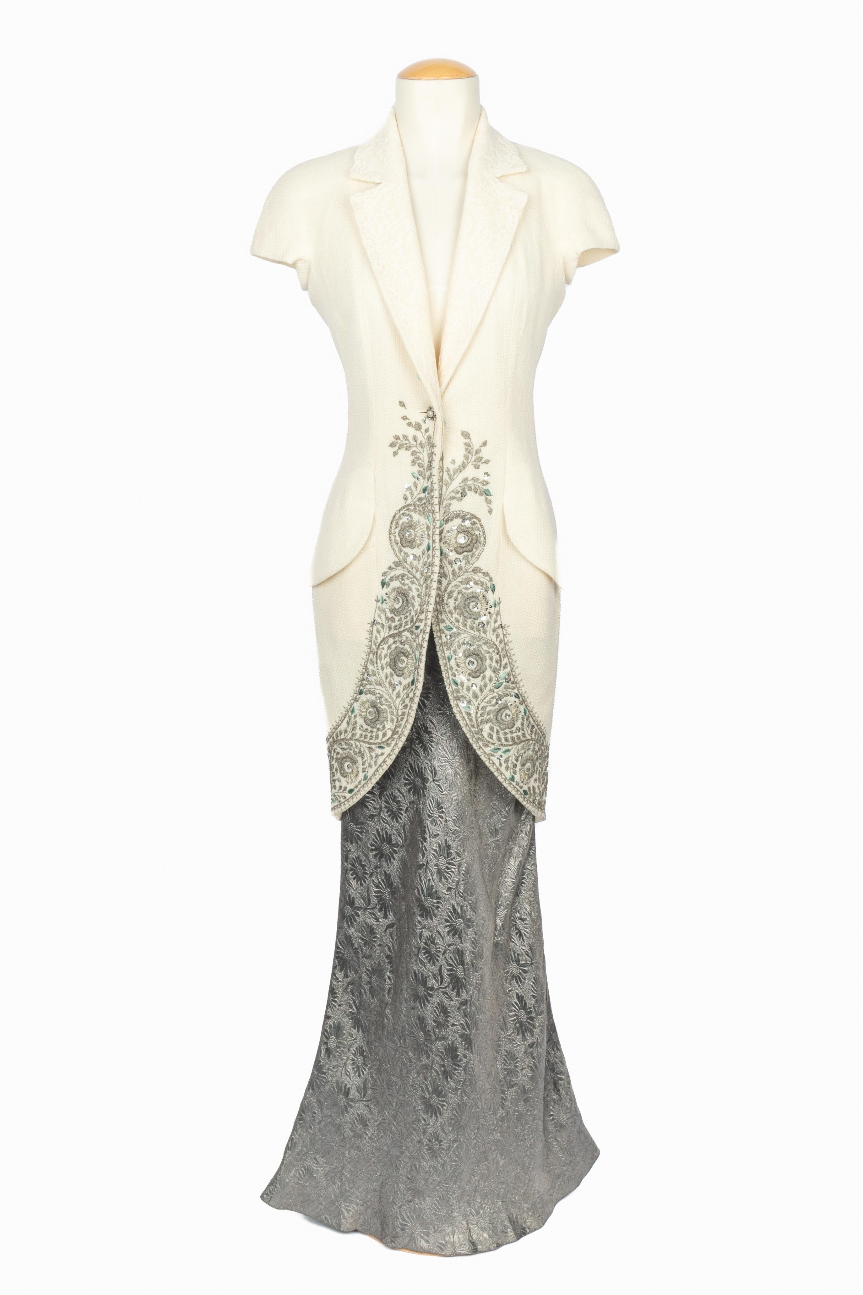 DIOR - (Fabricado en Francia) Conjunto compuesto por una chaqueta de lana blanca roto de manga corta, ribeteada con bordados de hilo de lúrex plateado y lentejuelas. Cuello adornado con encaje blanco. Falda larga de jacquard con motivo floral de