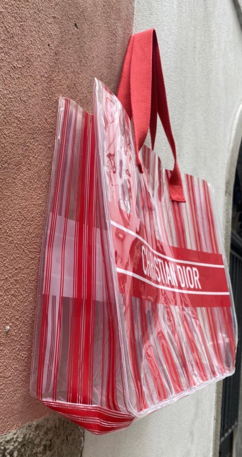 Transparent Christian Dior plastic shopping bag. Featuring red stripes and fabric’s handles. Measurements: base 41 cm, height 34 cm, depth 13 cm, handles height 20 cm, in good condition.