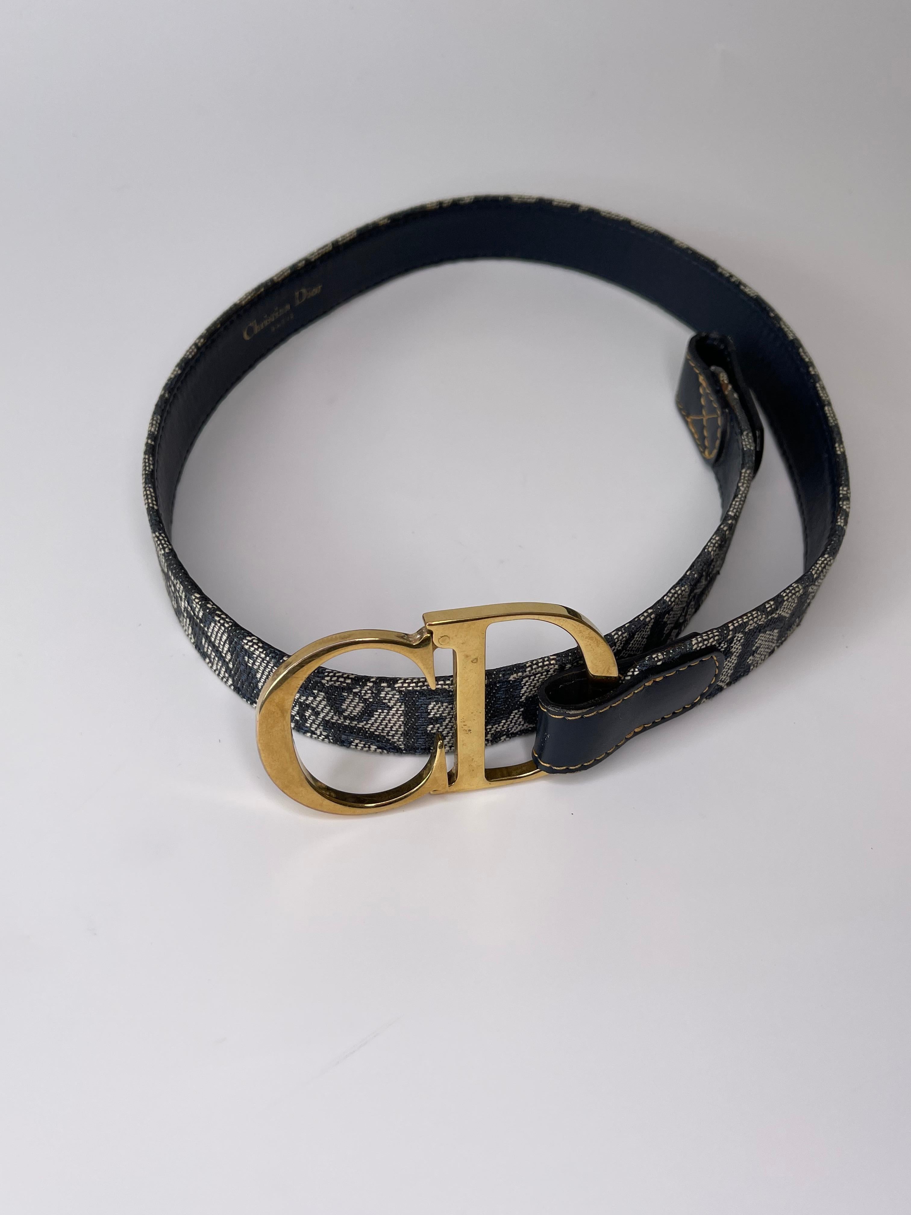 This Dior trotter pattern belt is made of leather and canvas and also consists of a large gold tone buckle, looks great in contrast to gold stitching at leather near the buckle itself. Dior logo located throughout the belt. 

COLOR: Navy
MATERIAL: