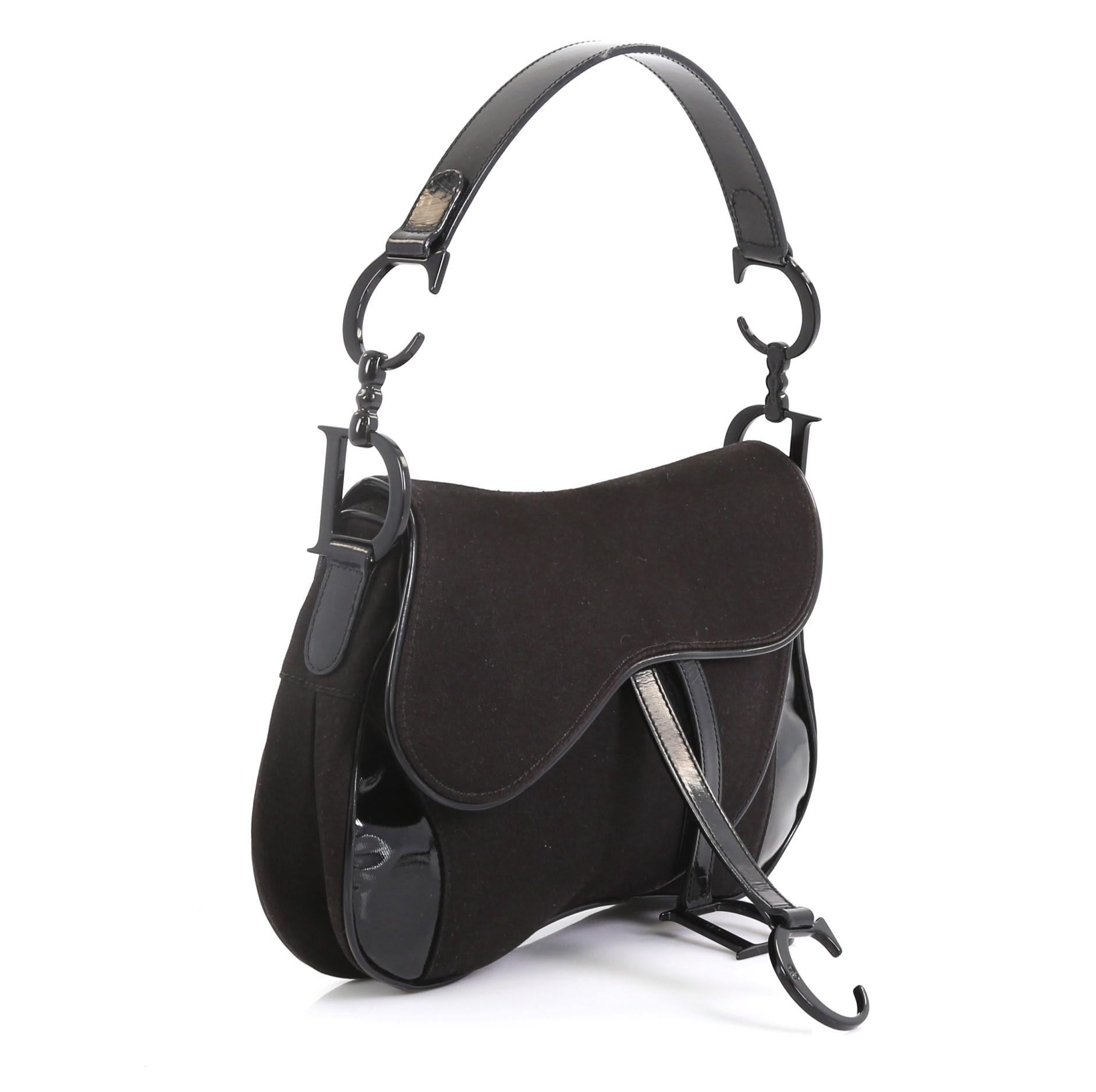 This Christian Dior Vintage Double Saddle Bag Canvas with Patent, crafted from black canvas and patent leather, features a top handle adorned with metal 'CD' finishing and black-tone hardware. Its fold over top opens to a black nylon interior with