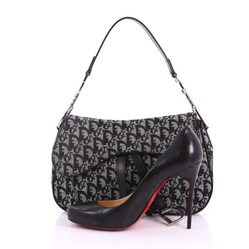 This Christian Dior Vintage Double Saddle Bag Diorissimo Canvas, crafted from black diorissimo canvas, features a top handle adorned with metal 'CD' finishing and silver-tone hardware. Its fold over top opens to a black fabric interior with zip