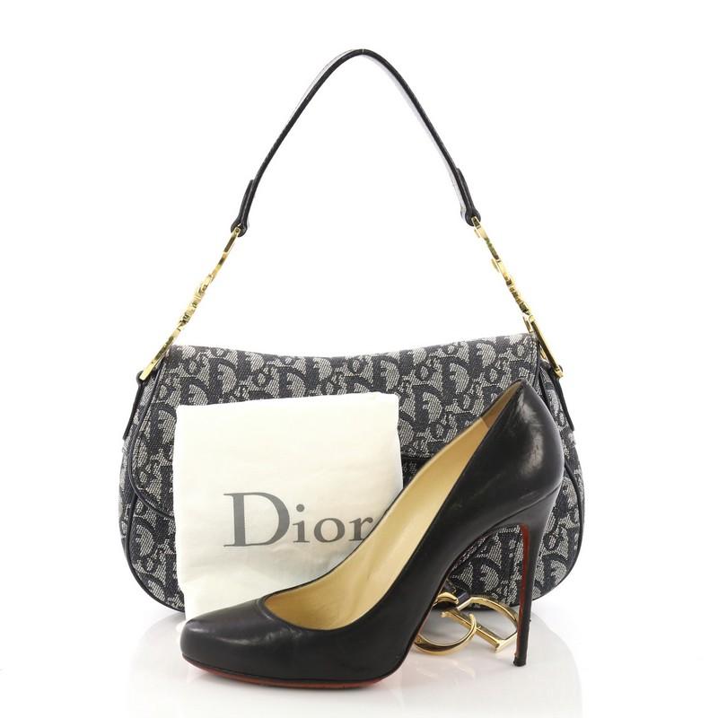  This Christian Dior Vintage Double Saddle Bag Diorissimo Canvas, crafted from blue diorissimo canvas, features a top handle adorned with metal 'CD' finishing and gold-tone hardware. Its fold over top opens to a navy fabric interior with zip pocket.