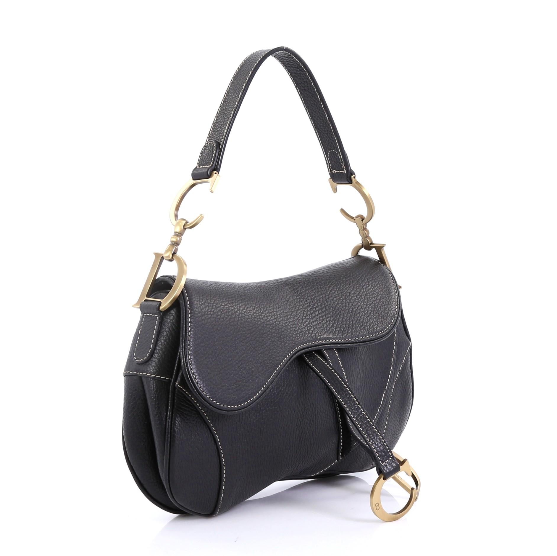 This Christian Dior Vintage Double Saddle Bag Leather, crafted from black leather, features a top handle adorned with metal 'CD' finishing and aged gold-tone hardware. Its fold over top opens to a black fabric interior with zip pocket. 

Condition: