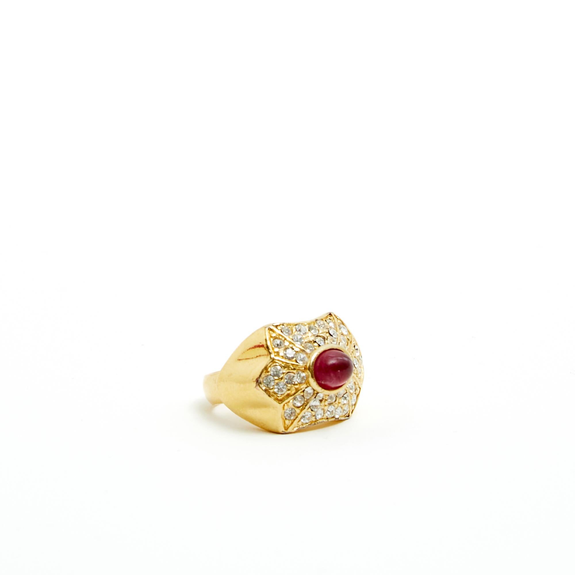 Ring von Christian Dior um 1990 im Art-déco-Stil aus goldenem Metall, besetzt mit Strasssteinen im Brillant-Stil und einem Stein, der einen Rubin imitiert, signiert. Fingergröße (auf Ringmaß) 49 oder US4,75, Innendurchmesser 1,57 cm, Maße des