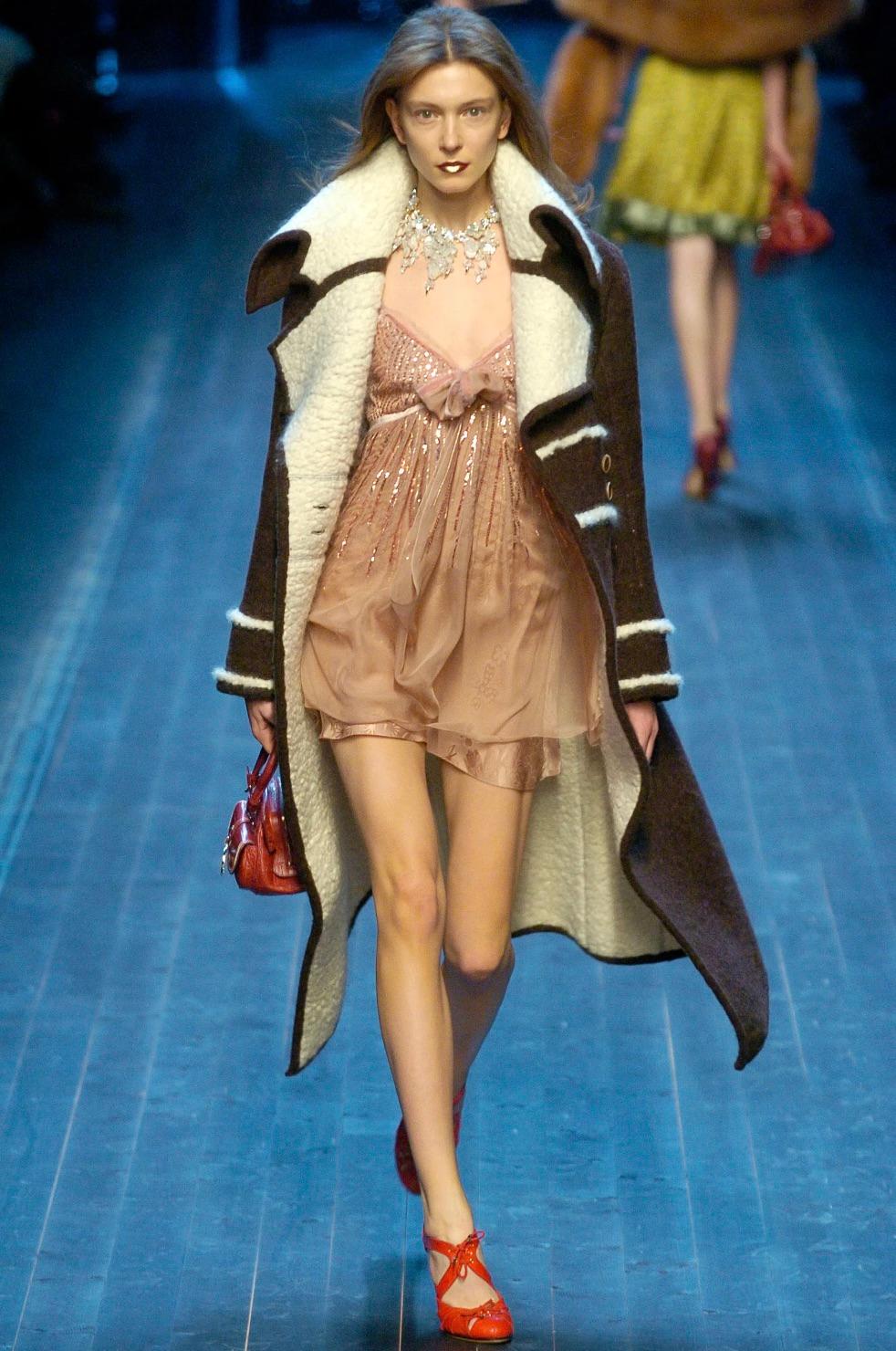 This mauve pink mini dress from Christian Dior by John Galliano’s Fall 2005 collection features delicate chiffon draping, a ruched bust with a velvet bow, and intricate gold sequin embellishments in an Art Deco-inspired pattern. With thin spaghetti