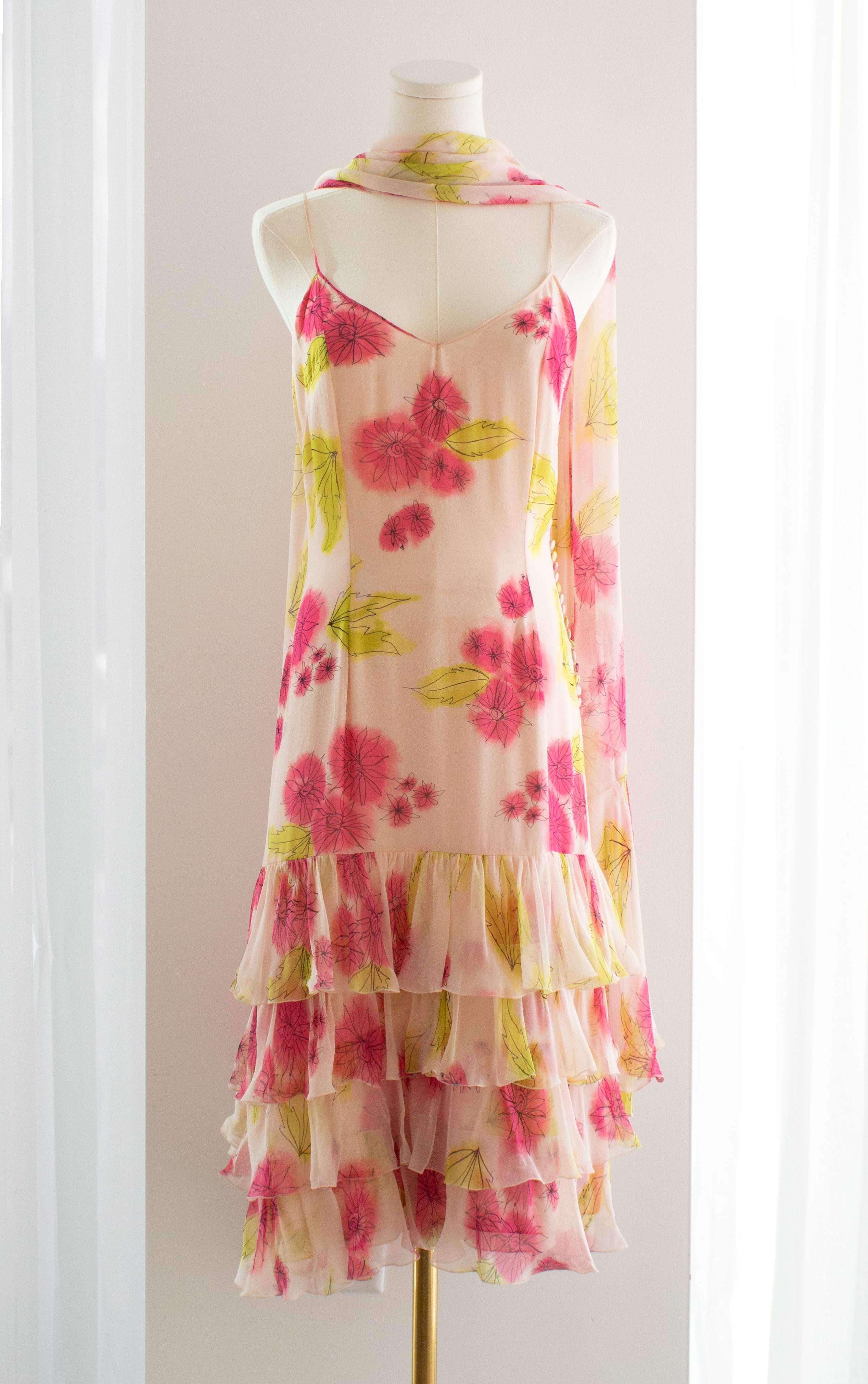 This is a stunning vintage Christian Dior dress designed by John Galliano. The dress features a delicate and ethereal floral print in shades of pink and green on a soft, sheer fabric, creating a dreamy and romantic aesthetic. It has a flattering