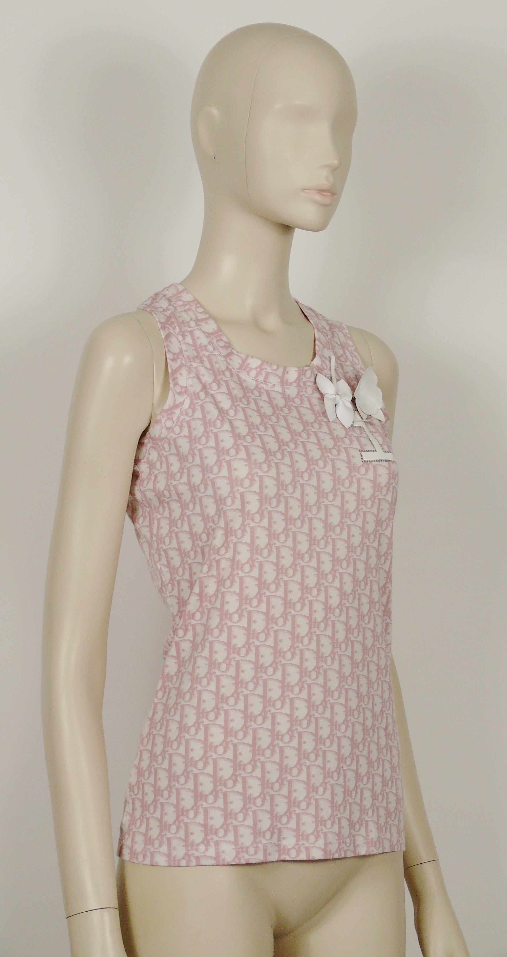 Vintage-Tank-Top von CHRISTIAN DIOR by JOHN GALLIANO mit Monogramm-Muster in mädchenhaftem Rosa auf weißem Hintergrund, 2 weißen Blumenbroschen aus Lack und einem kristallverzierten Nº1-Aufnäher auf der Brust.

Auf dem Label steht CHRISTIAN DIOR